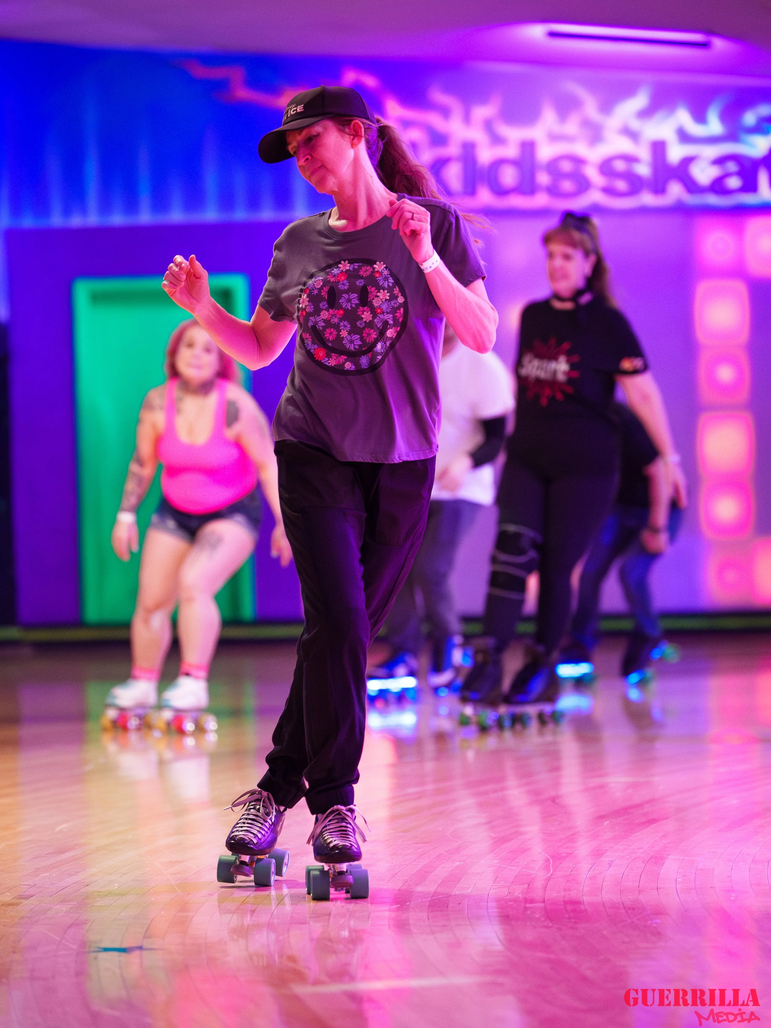 Multiple women roller skating in a roller disco with colorful neon lighting.