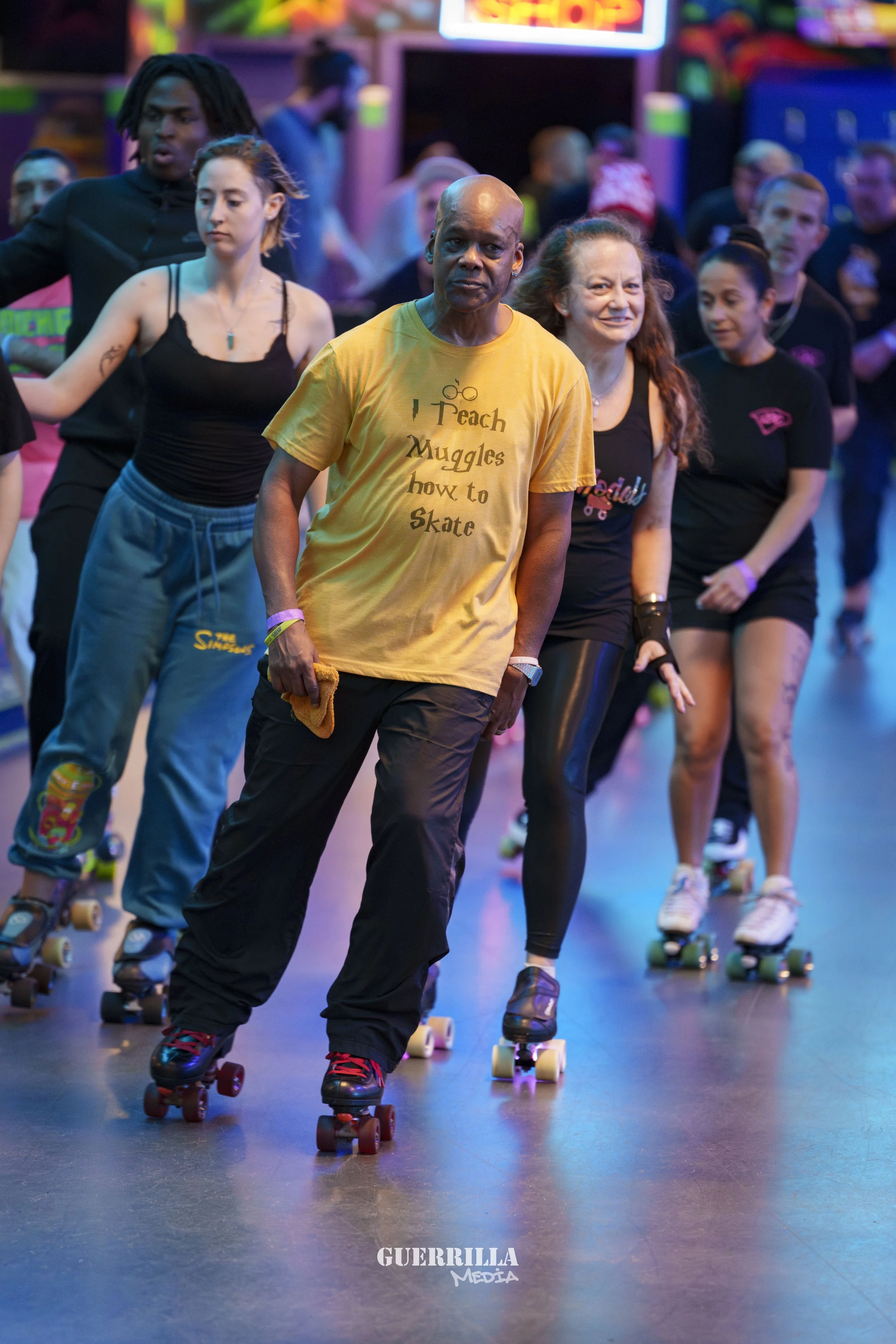 Group of people roller skating in a colorful indoor rink, with a neon sign in the background, some wearing skate gear and casual clothes.