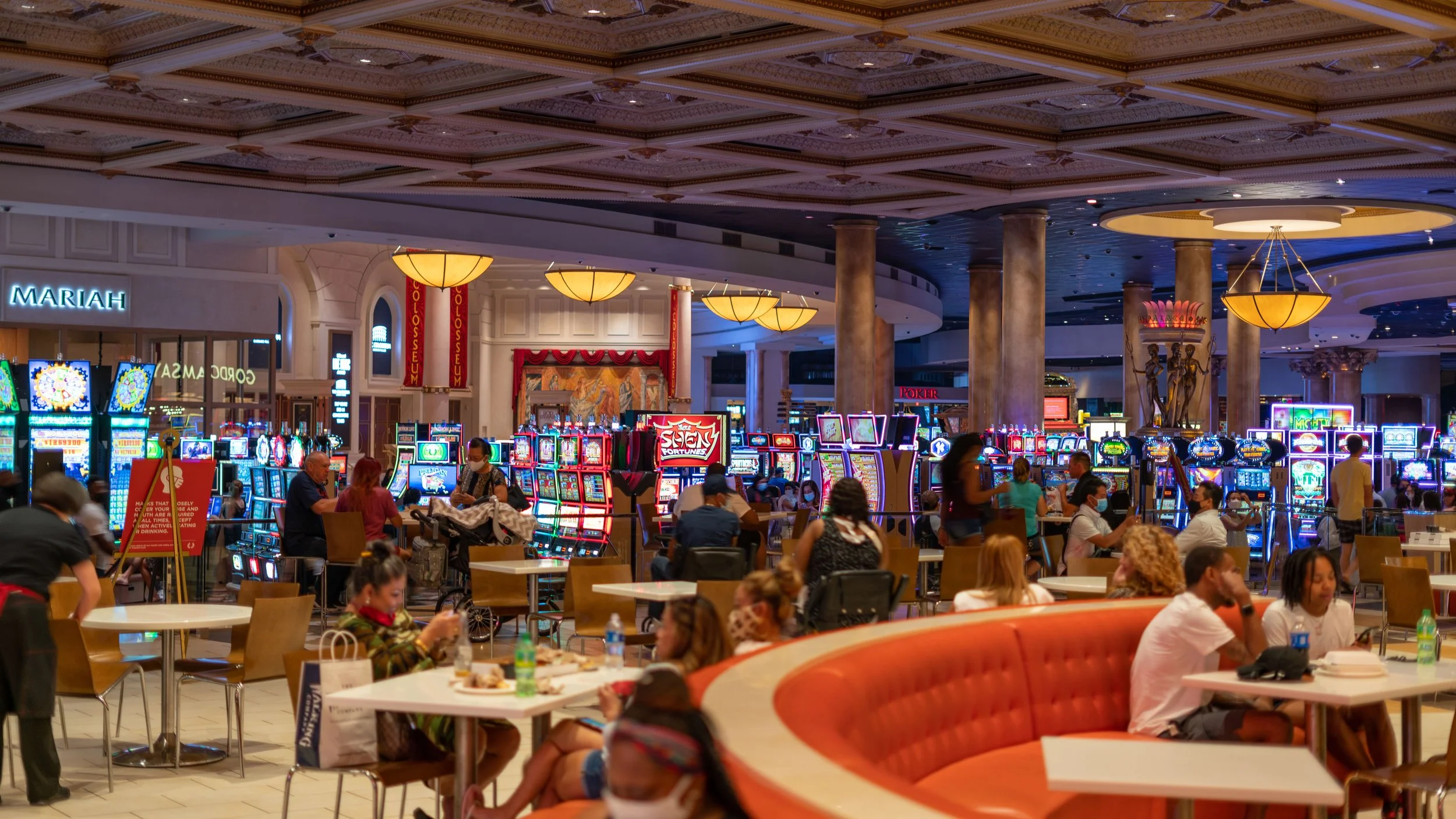 Inside a casino with slot machines, people sitting and playing or eating, and decorative lighting and sculptures.