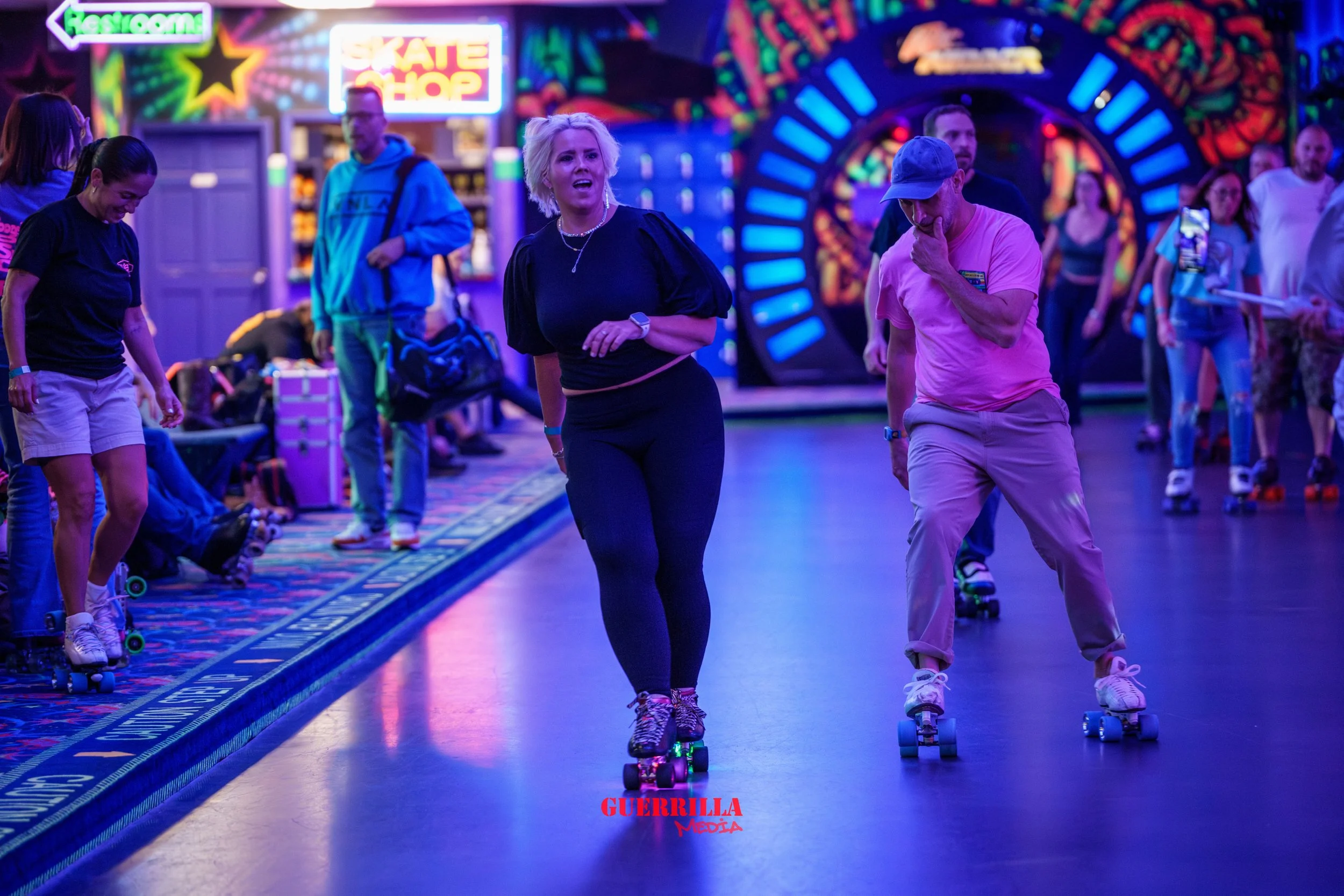 People roller skating inside an arcade with neon lights and colorful decorations.