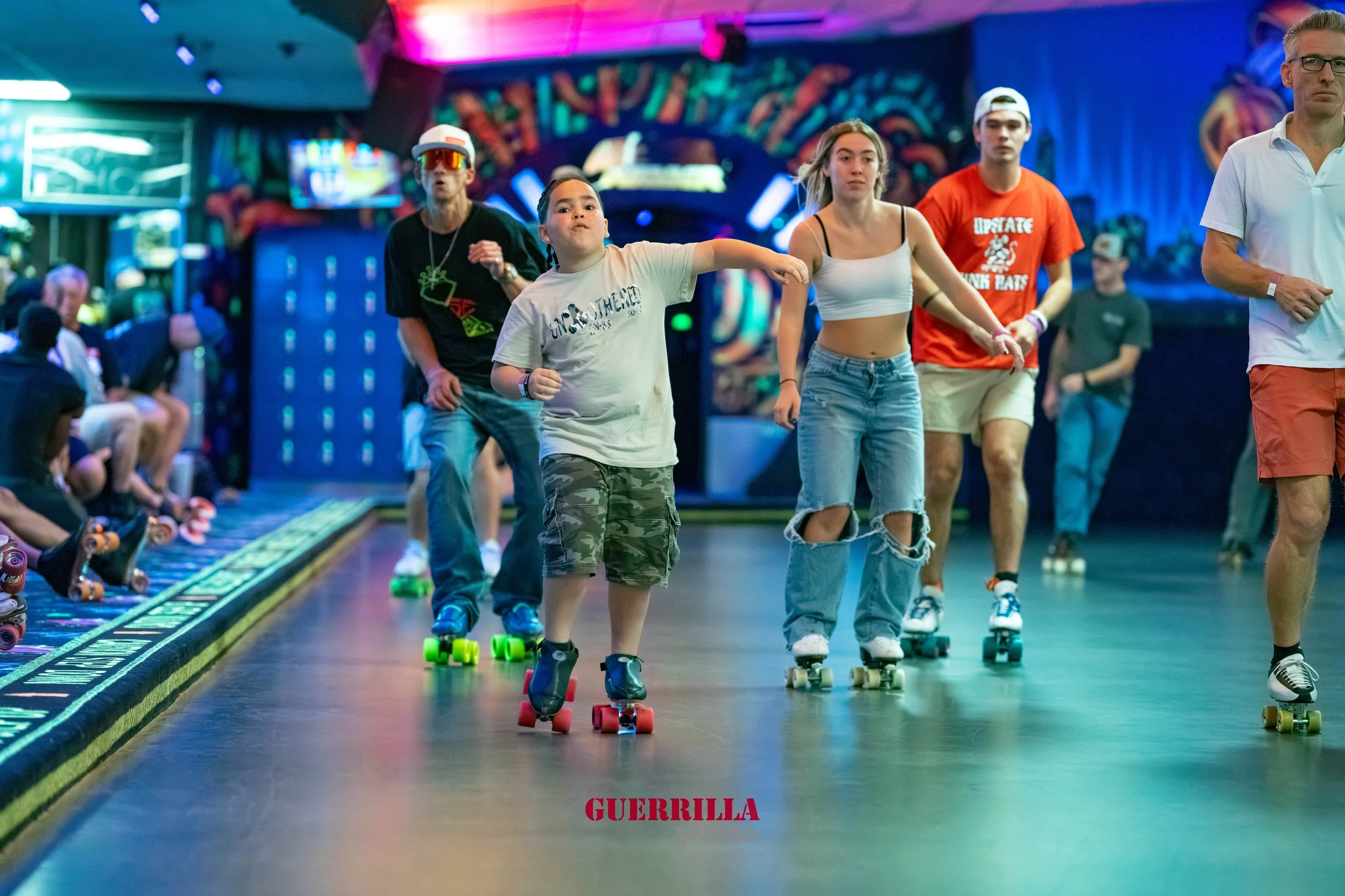 People roller skating inside a roller rink with colorful lighting and a vibrant backdrop.