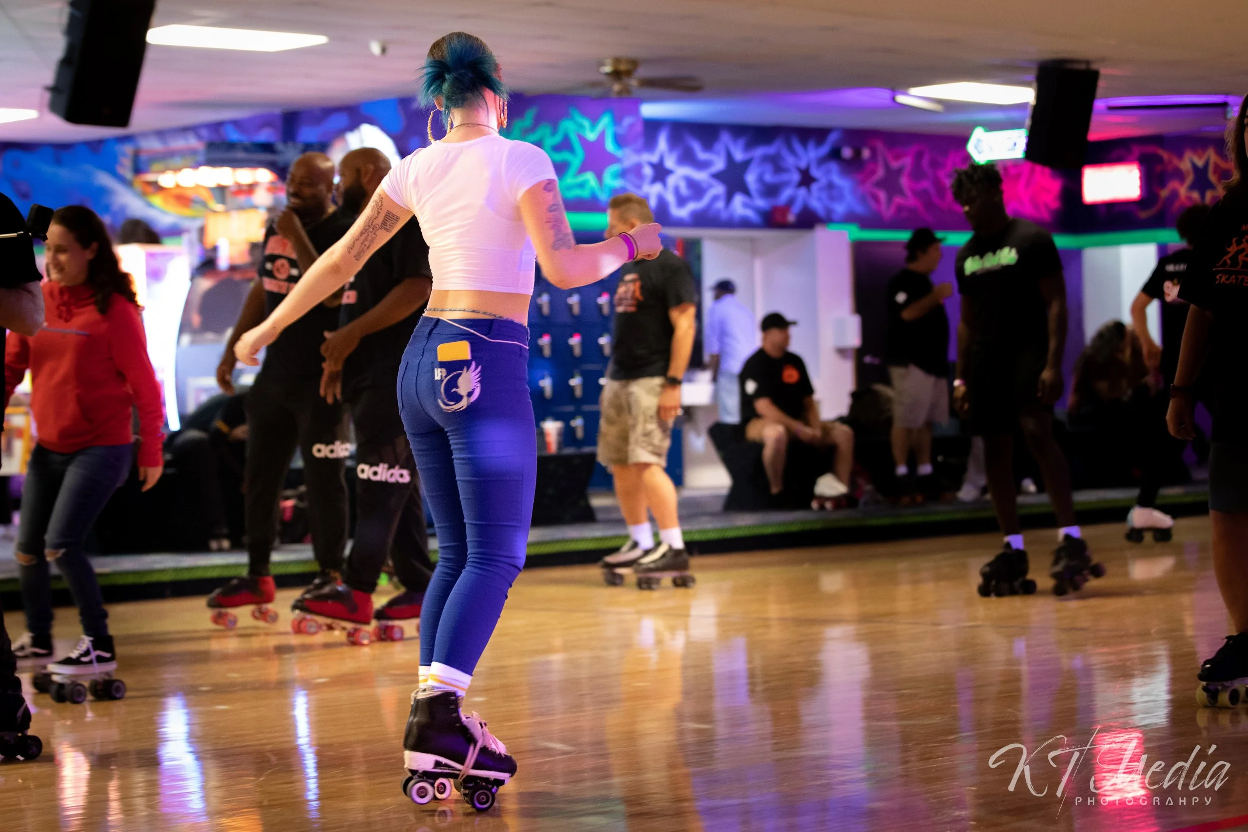 People roller skating in an indoor rink with colorful neon lights and murals.