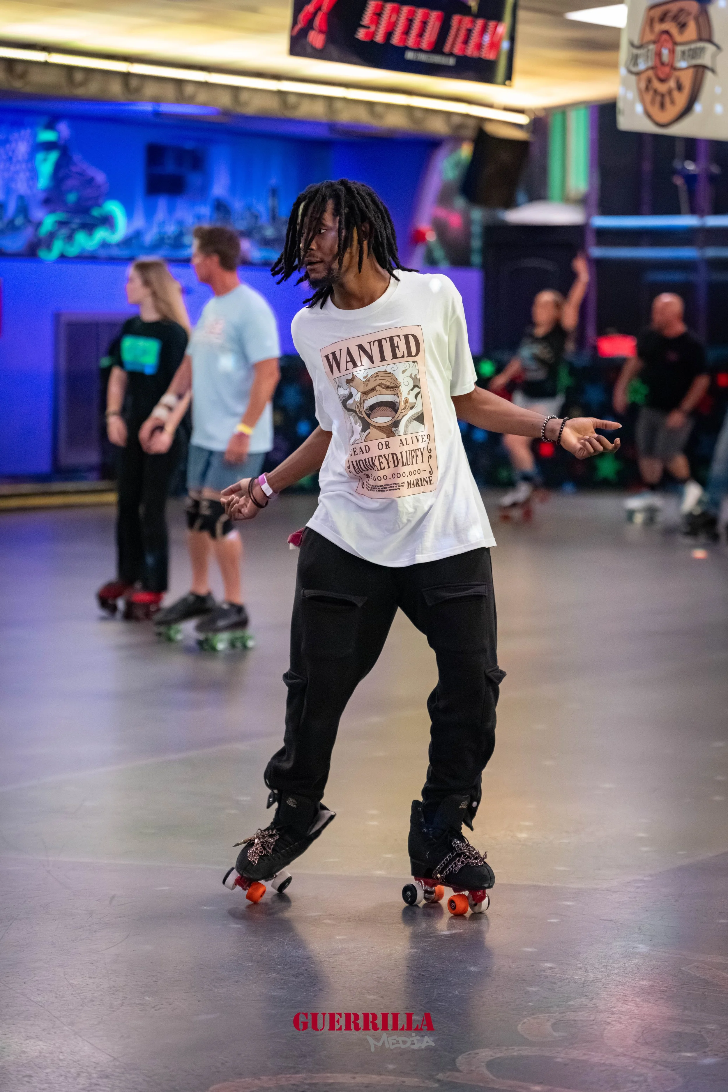 A man with dreadlocks roller skating indoors at a venue with neon lights, wearing a white t-shirt with a wanted poster print.