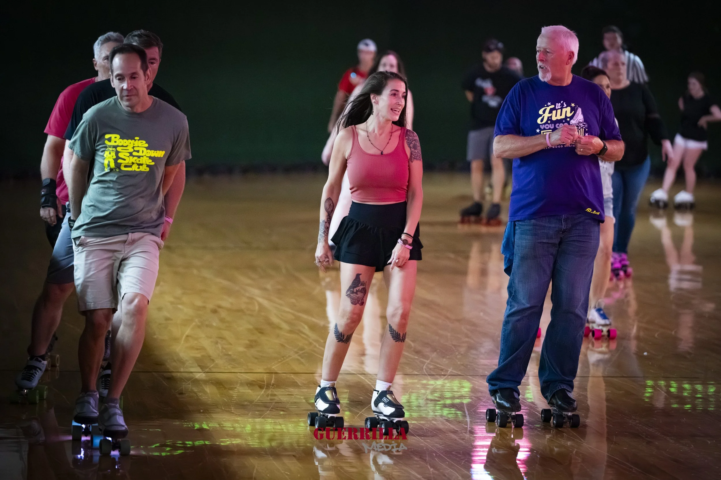 People roller skating indoors, with a woman in the center smiling and talking to an older man, surrounded by others skating in the background.
