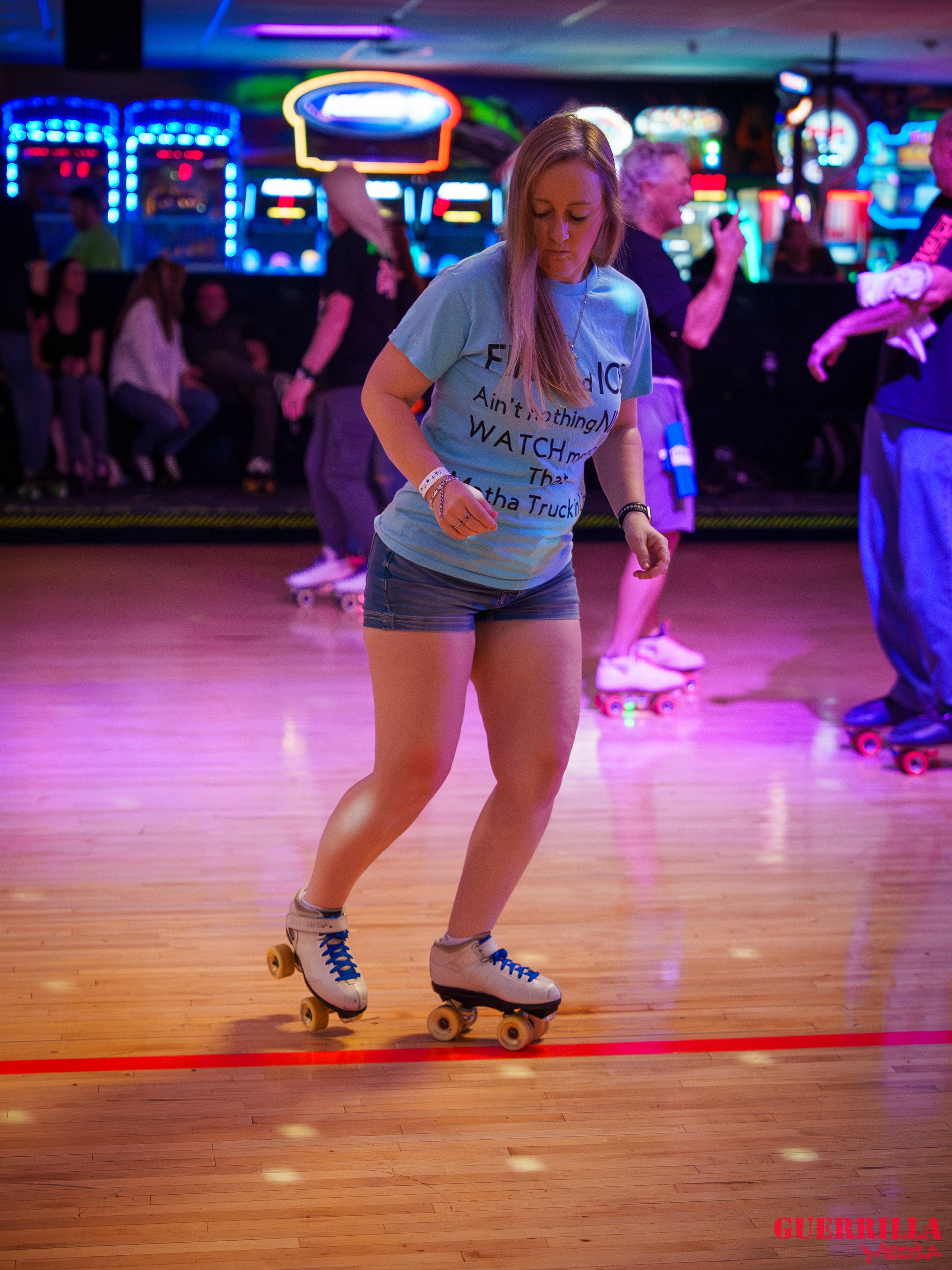 A woman rollerskating on a wooden rink with neon lights from arcade games in the background.