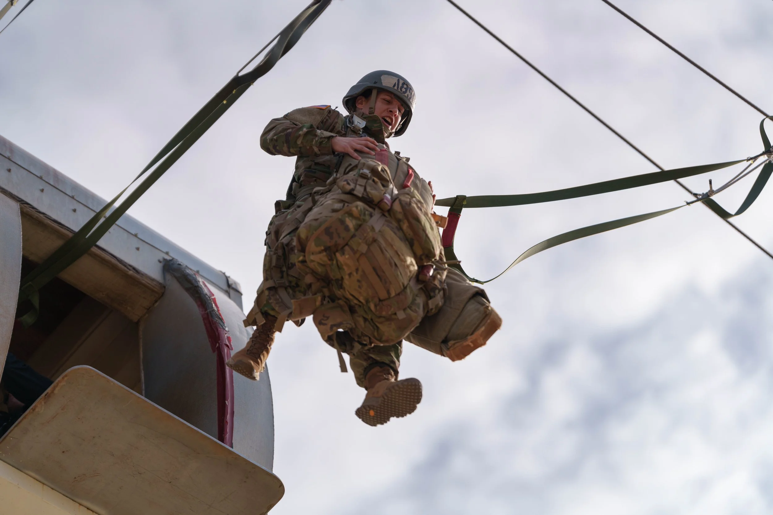Military personnel jumping out of a helicopter during a training exercise, wearing camouflage uniform and helmet.