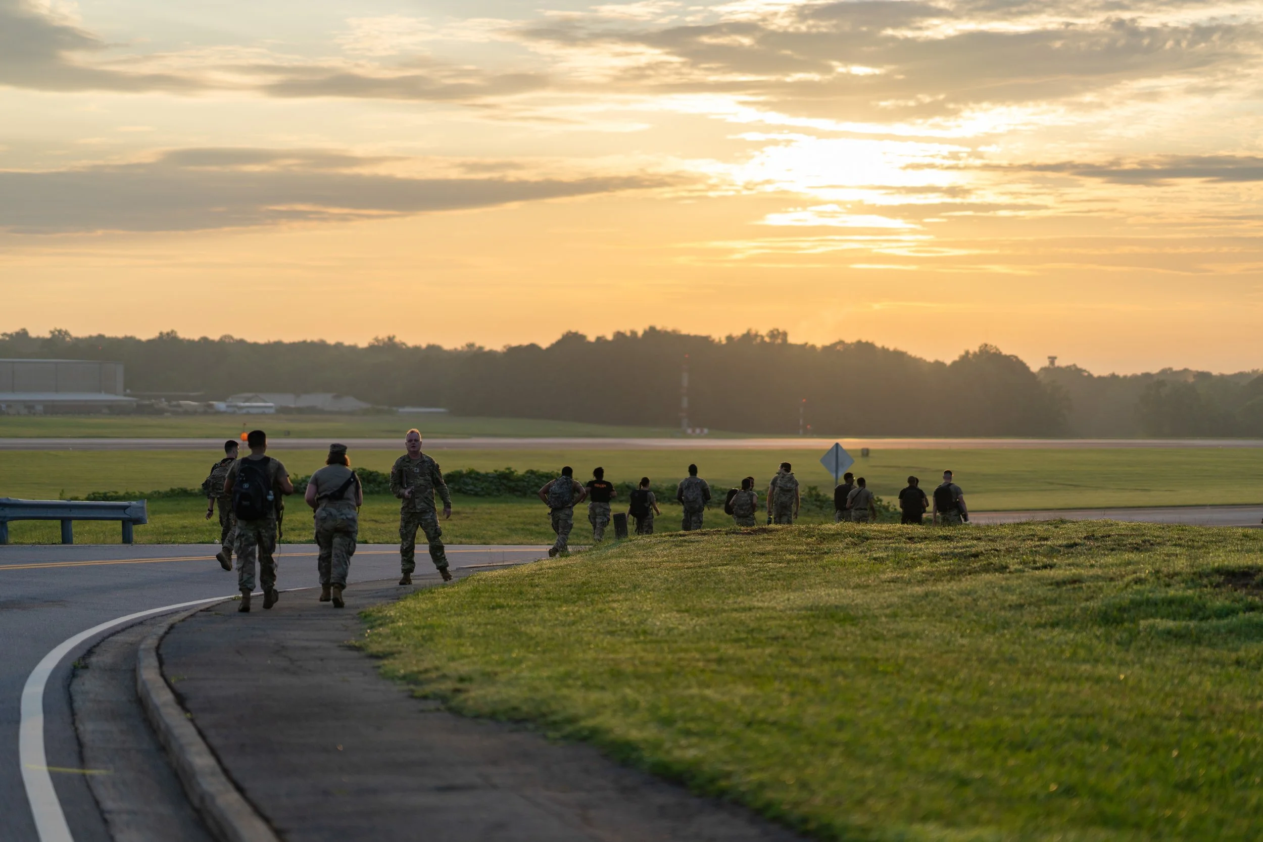 Soldiers walking and standing on a runway during sunset at an airport.