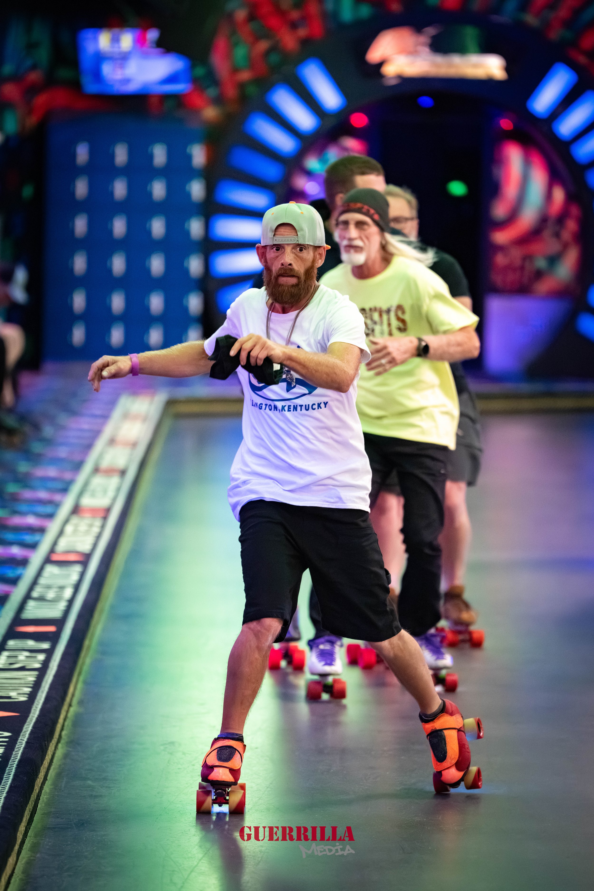Four men roller skating in an indoor skate rink with colorful lighting.