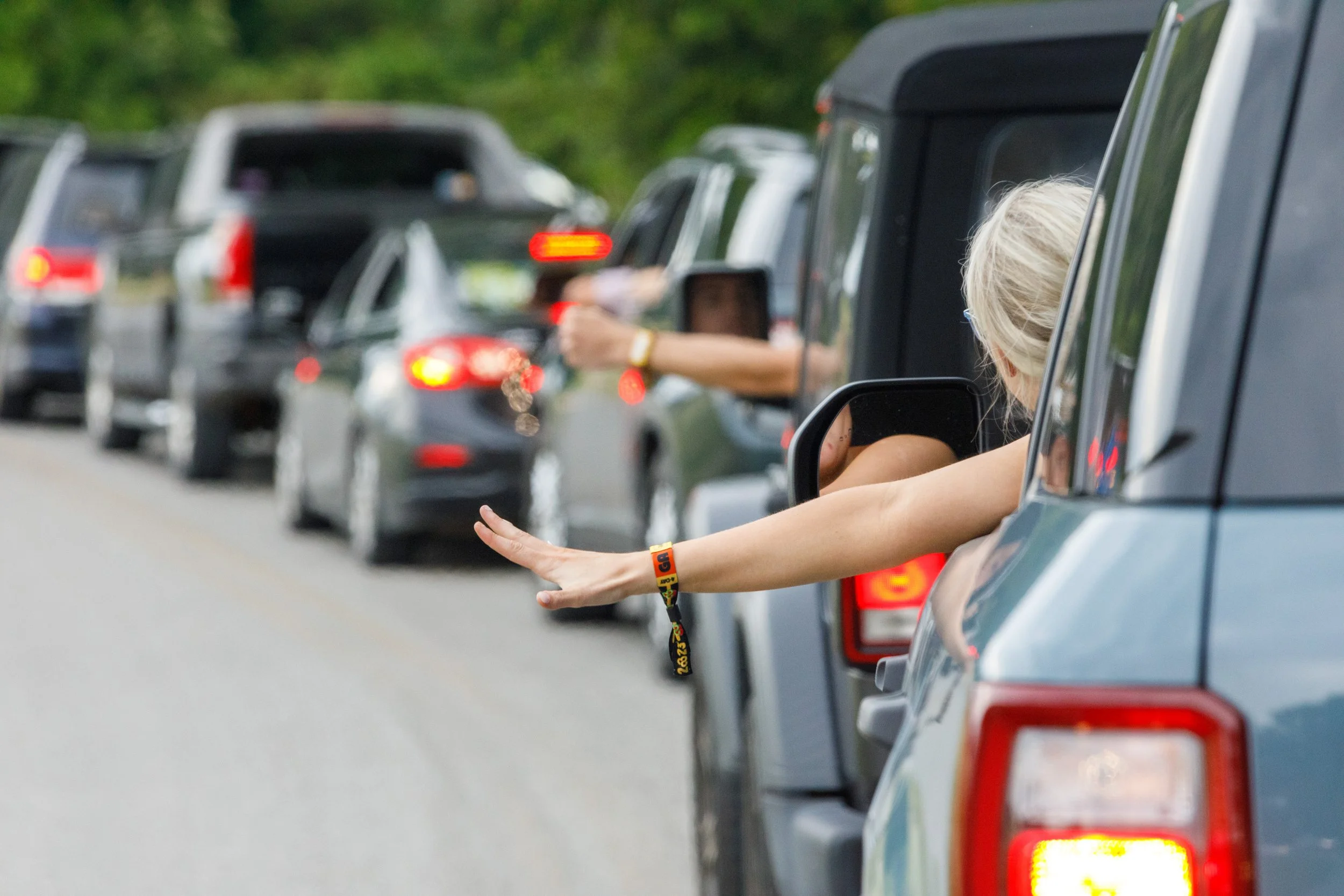 Line of cars on a road with a woman sticking her arm out of the car window, waving or signaling.