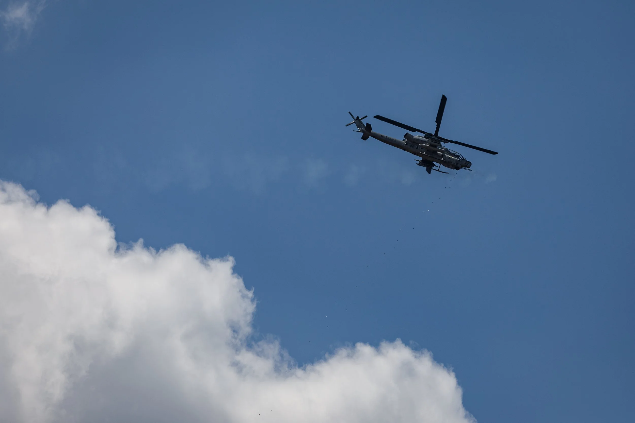A military helicopter flying in the sky near white clouds.