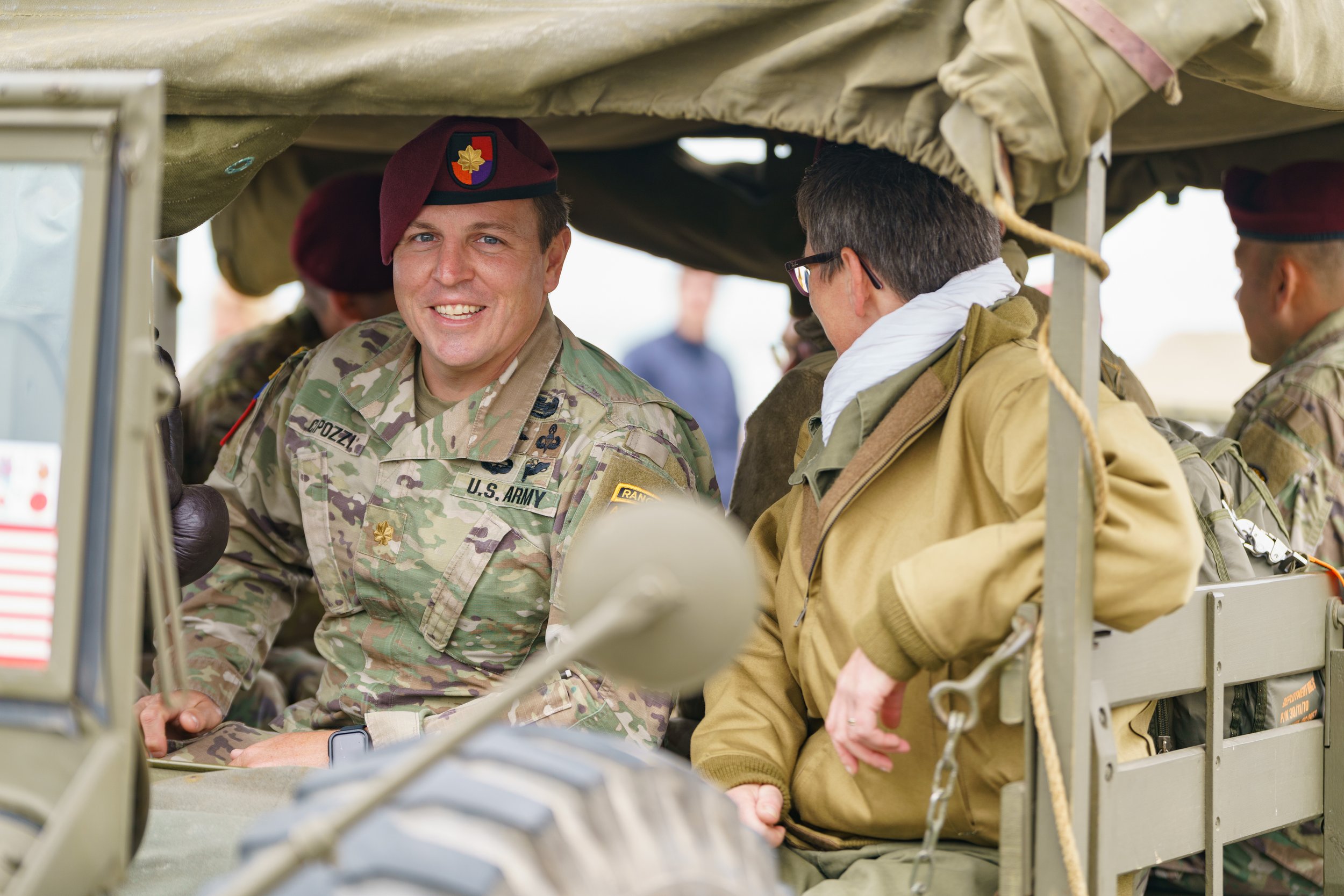 U.S. Army soldiers in camouflage uniforms and maroon berets sitting in a military vehicle, smiling and talking.