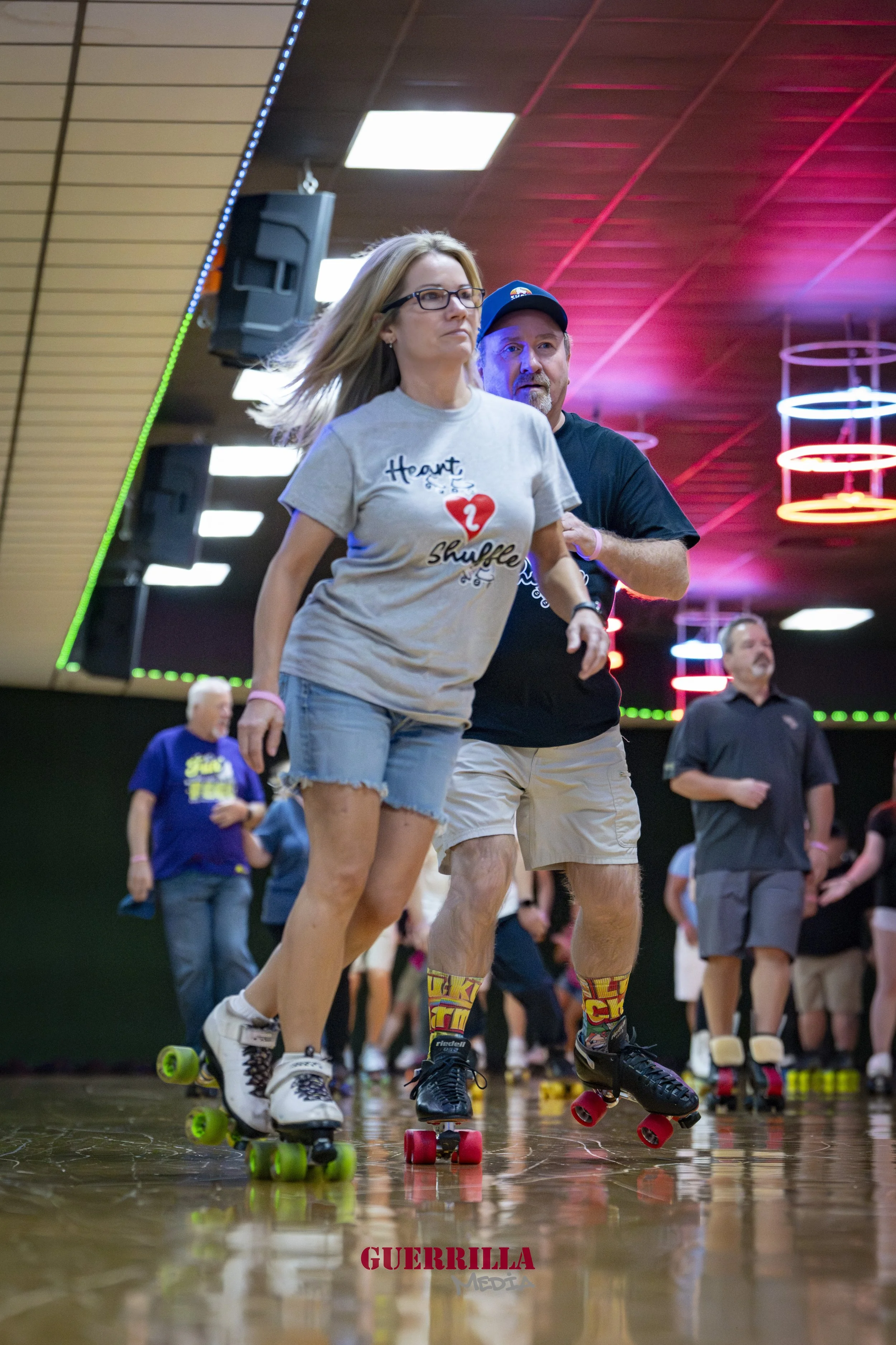 People roller skating indoors at a roller rink with colorful lighting and other skaters in the background.