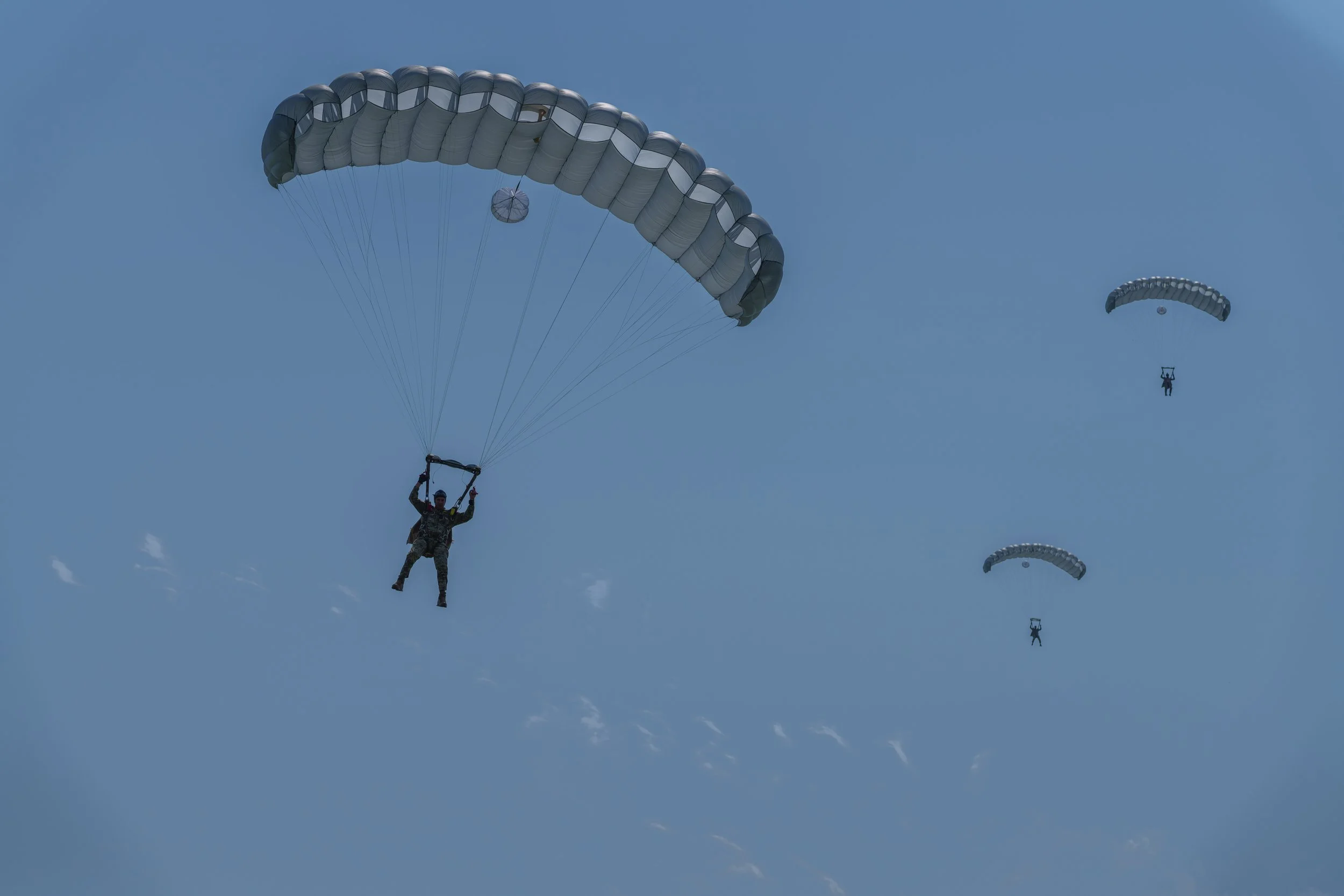 Three parachutists descending through the sky with their parachutes deployed.