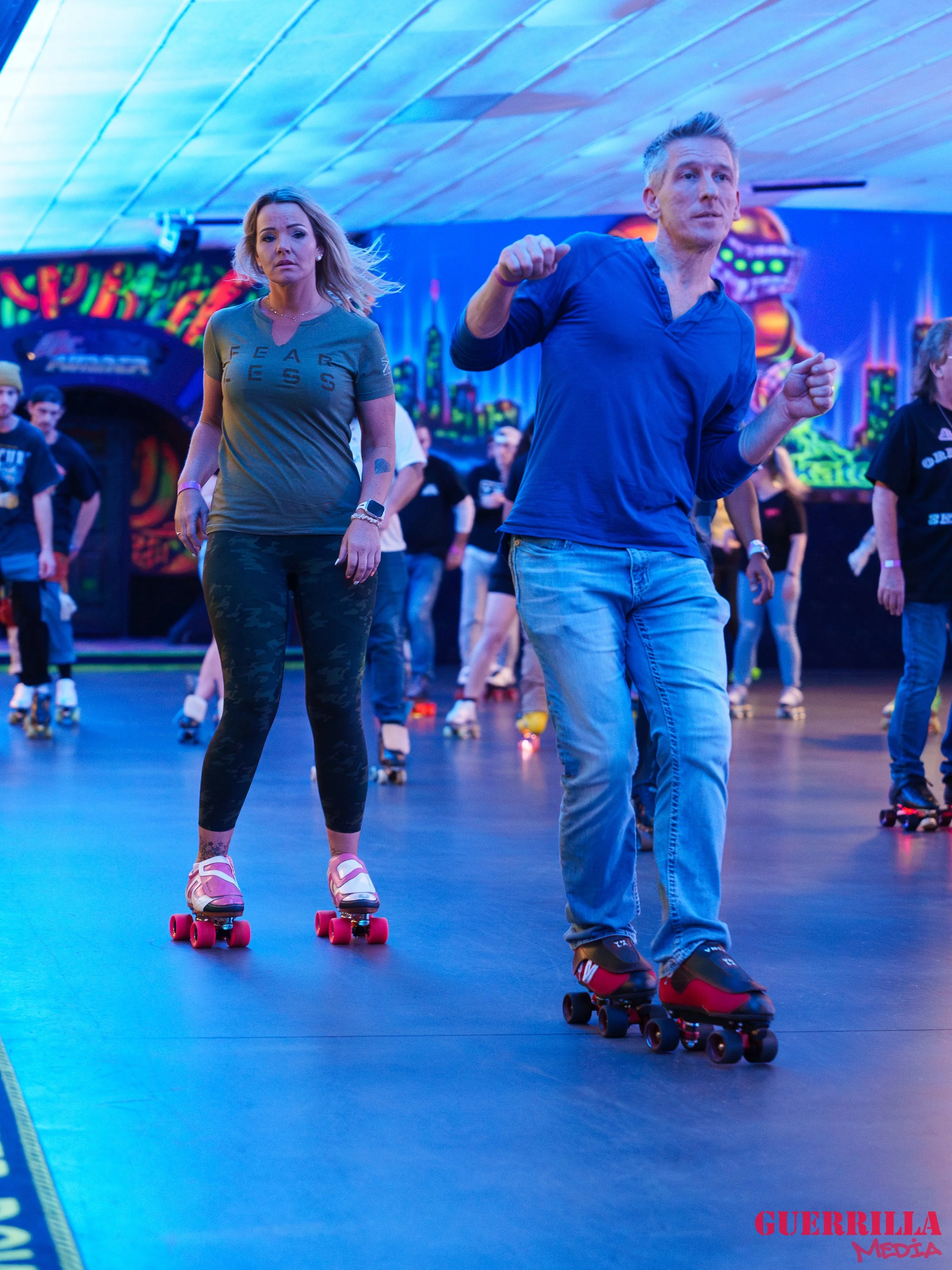 People roller skating indoors with neon lights and colorful graffiti in the background.