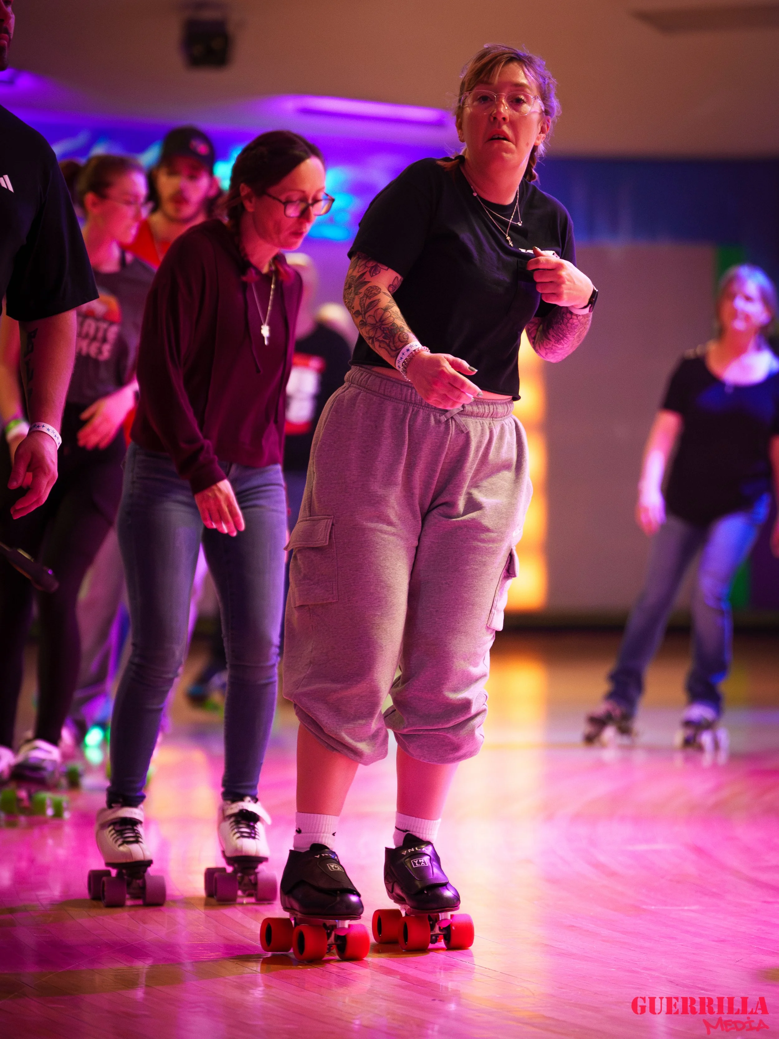 People roller-skating indoors, with colorful lighting, on a polished wooden floor.