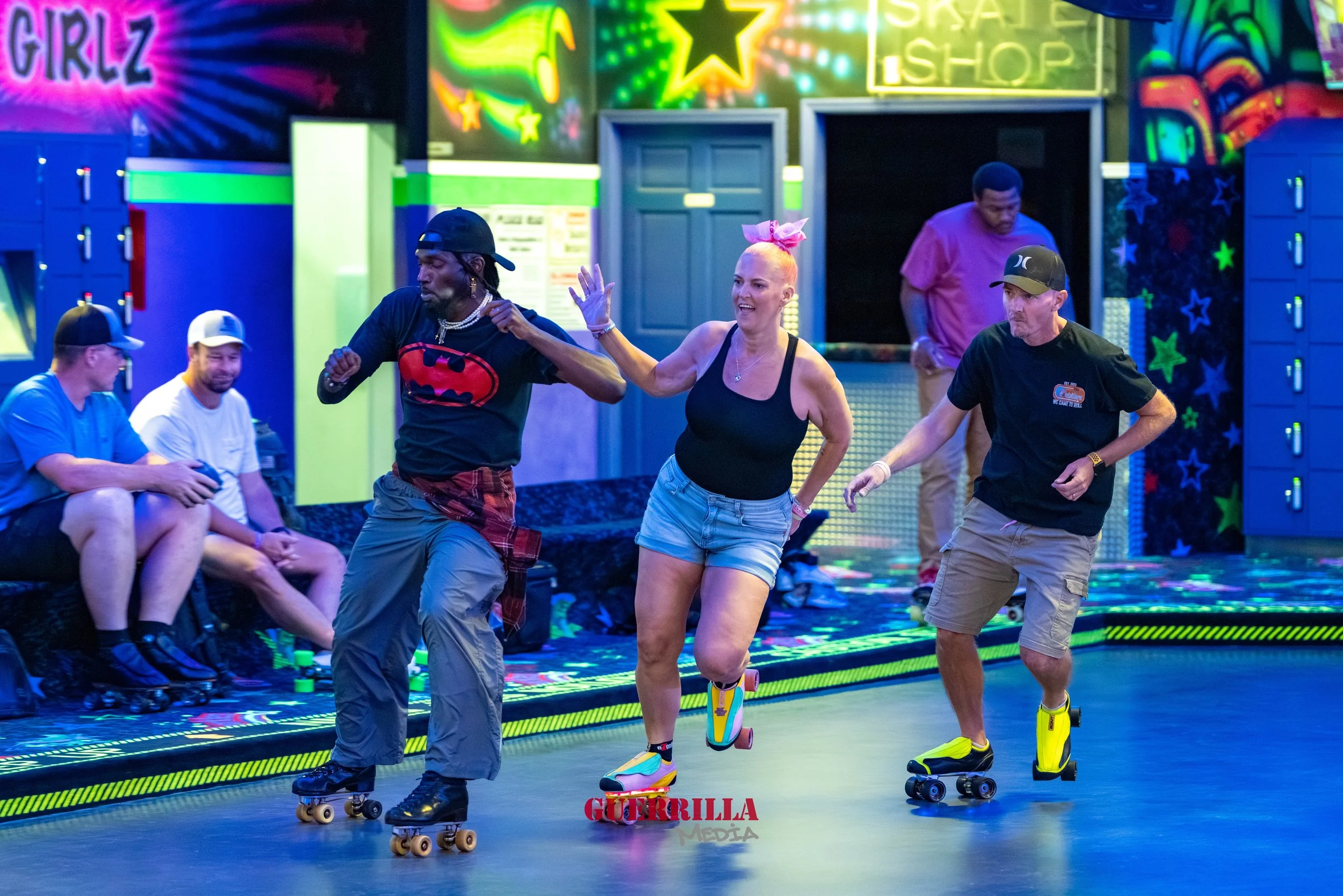 A group of people roller skating in an arcade or roller rink with neon lights and colorful decorations, including lockers and vibrant wall art.
