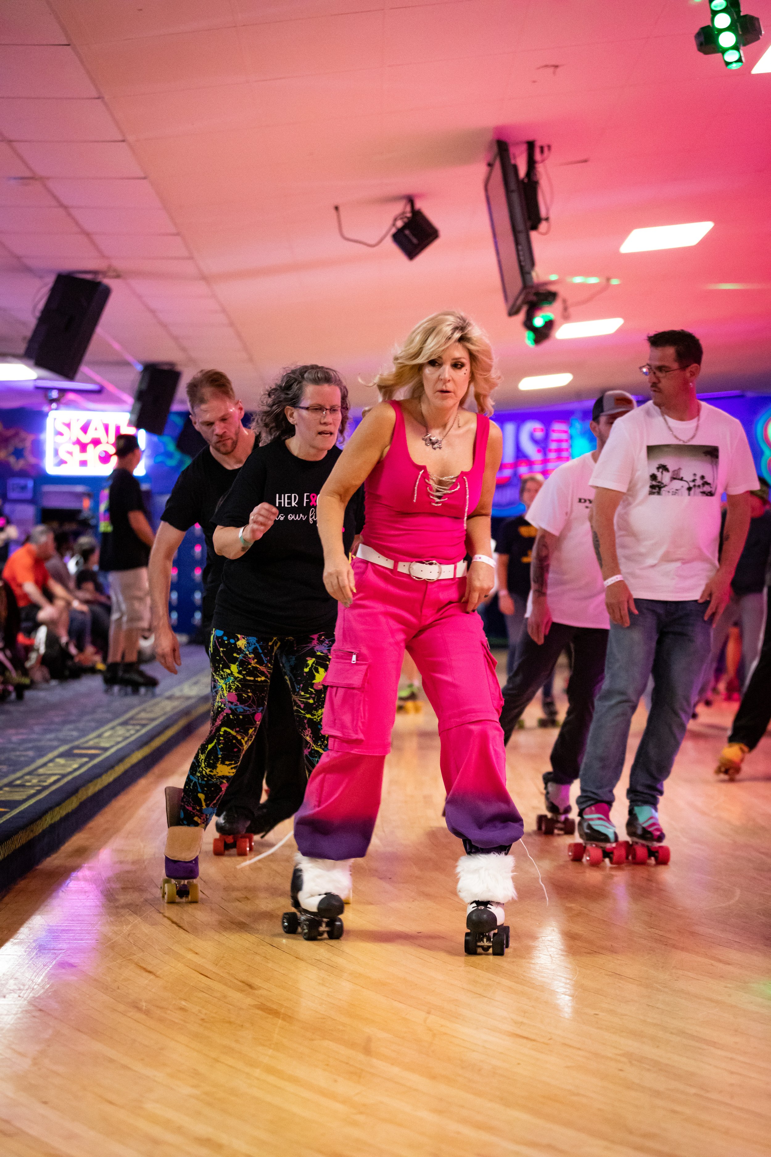 People rollerskating indoors at an event with colorful lights and a skate shop sign in the background.