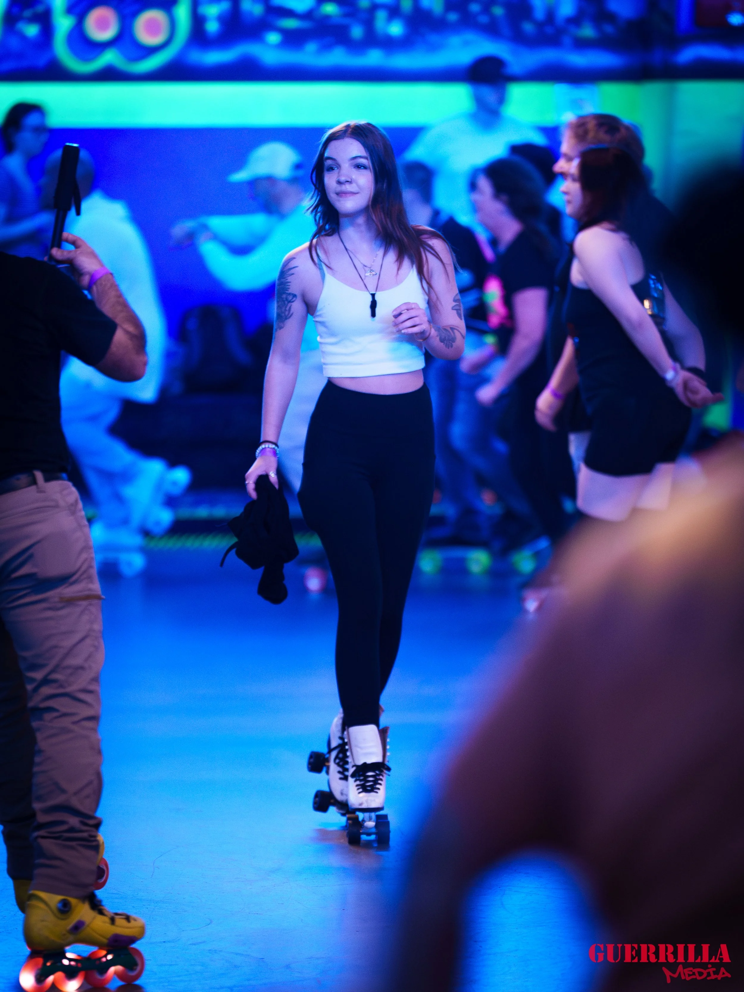 A woman roller skating in a neon-lit roller rink with other skaters in the background.