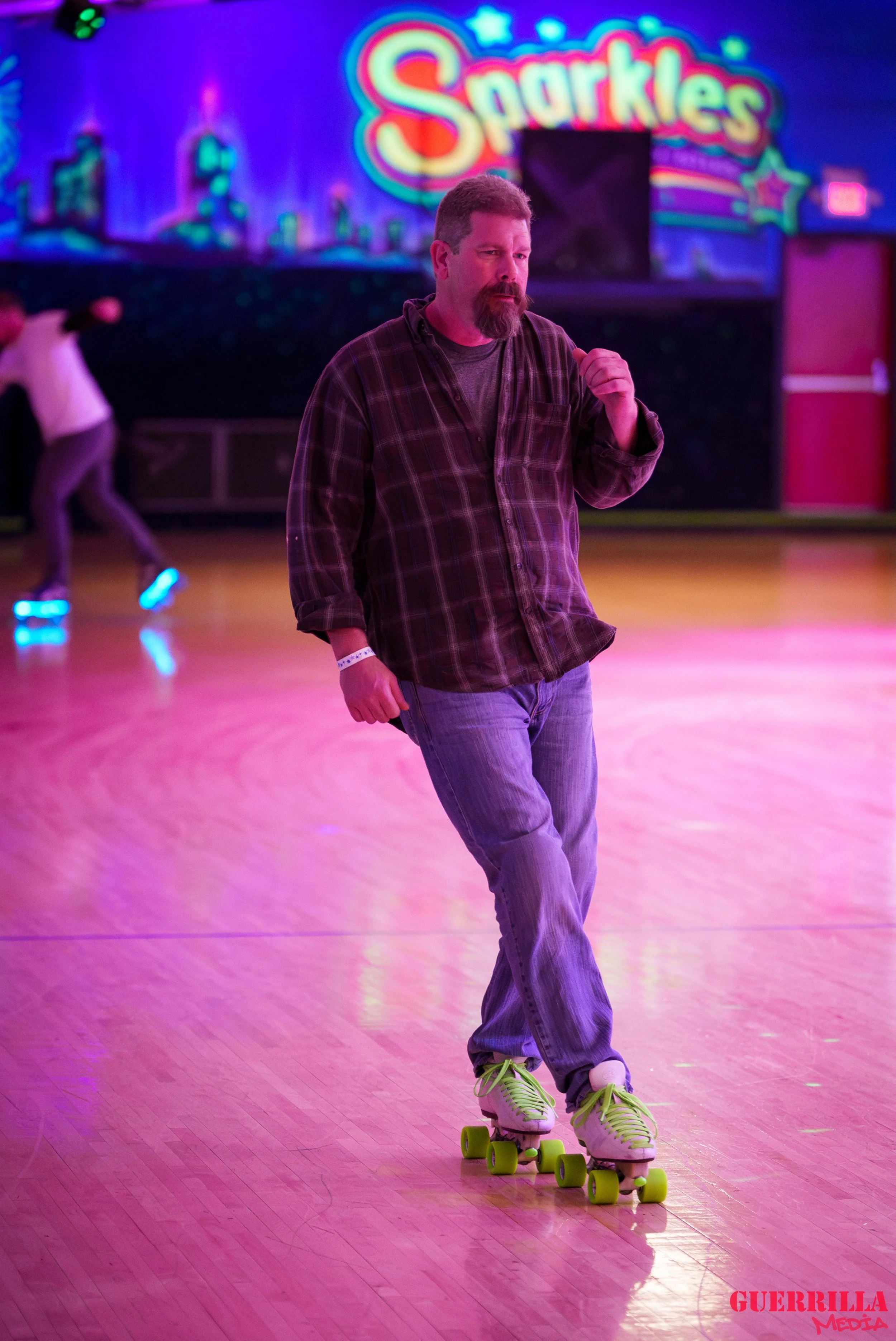 A man roller-skating in a neon-lit roller rink with a bright sign that reads 'Sparkles' in the background.