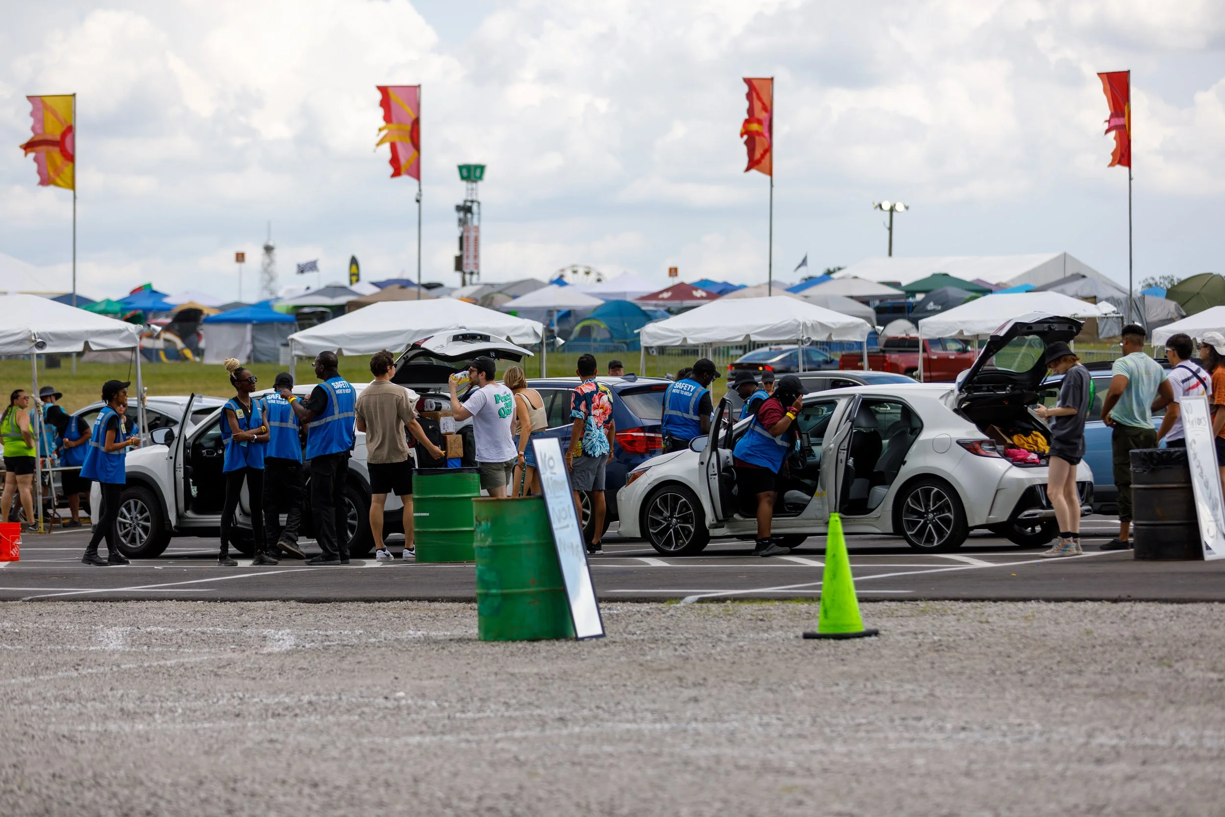 People check cars at an outdoor event with tents and flags in the background.
