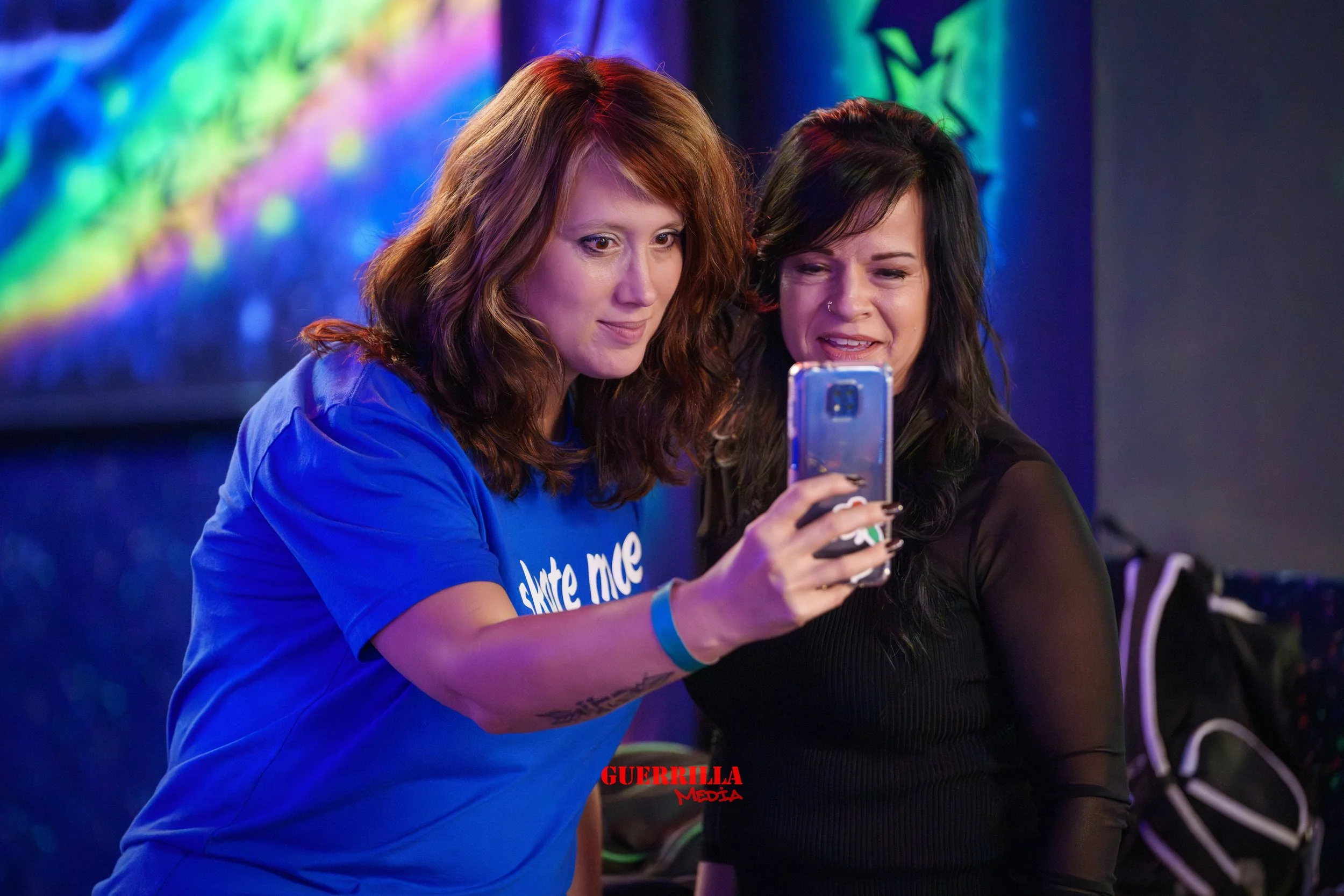 Two women taking a selfie together at a colorful, neon-lit venue.