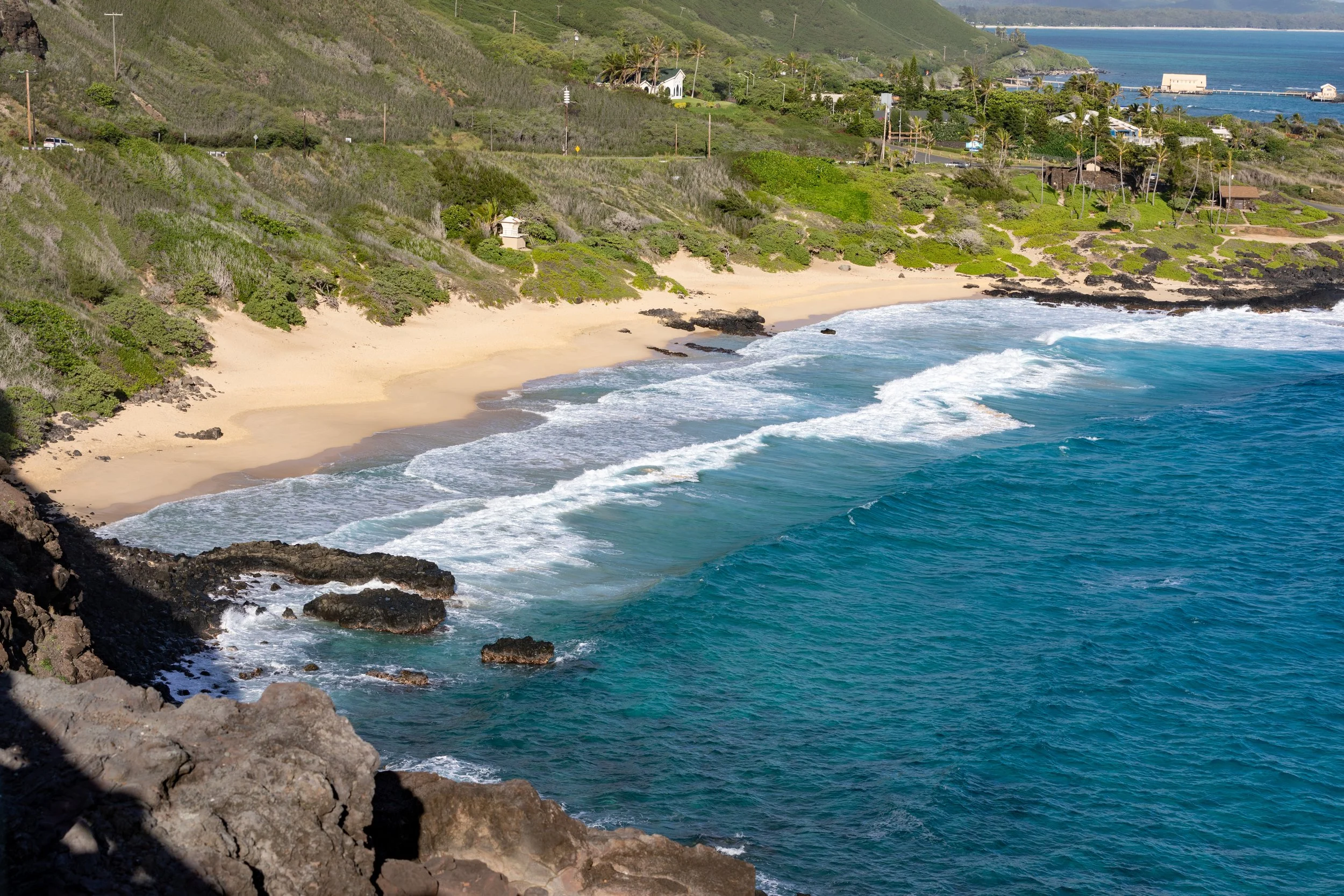 A scenic view of a secluded beach with golden sand, surrounded by rocky cliffs and lush green vegetation, with turquoise ocean waves gently crashing onto the shore.