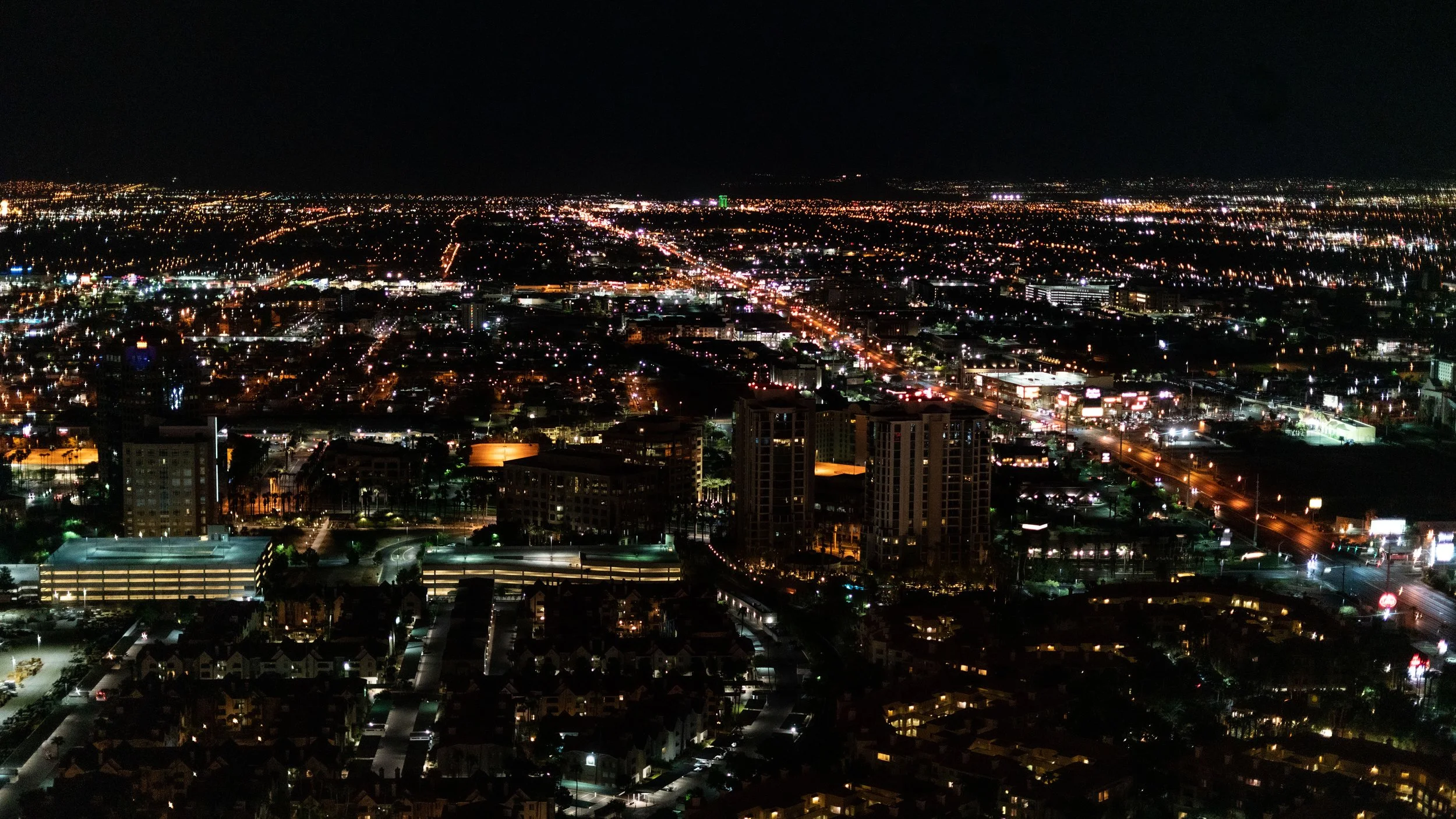 Nighttime aerial view of a city with illuminated buildings, streets, and highways stretching into the distance.