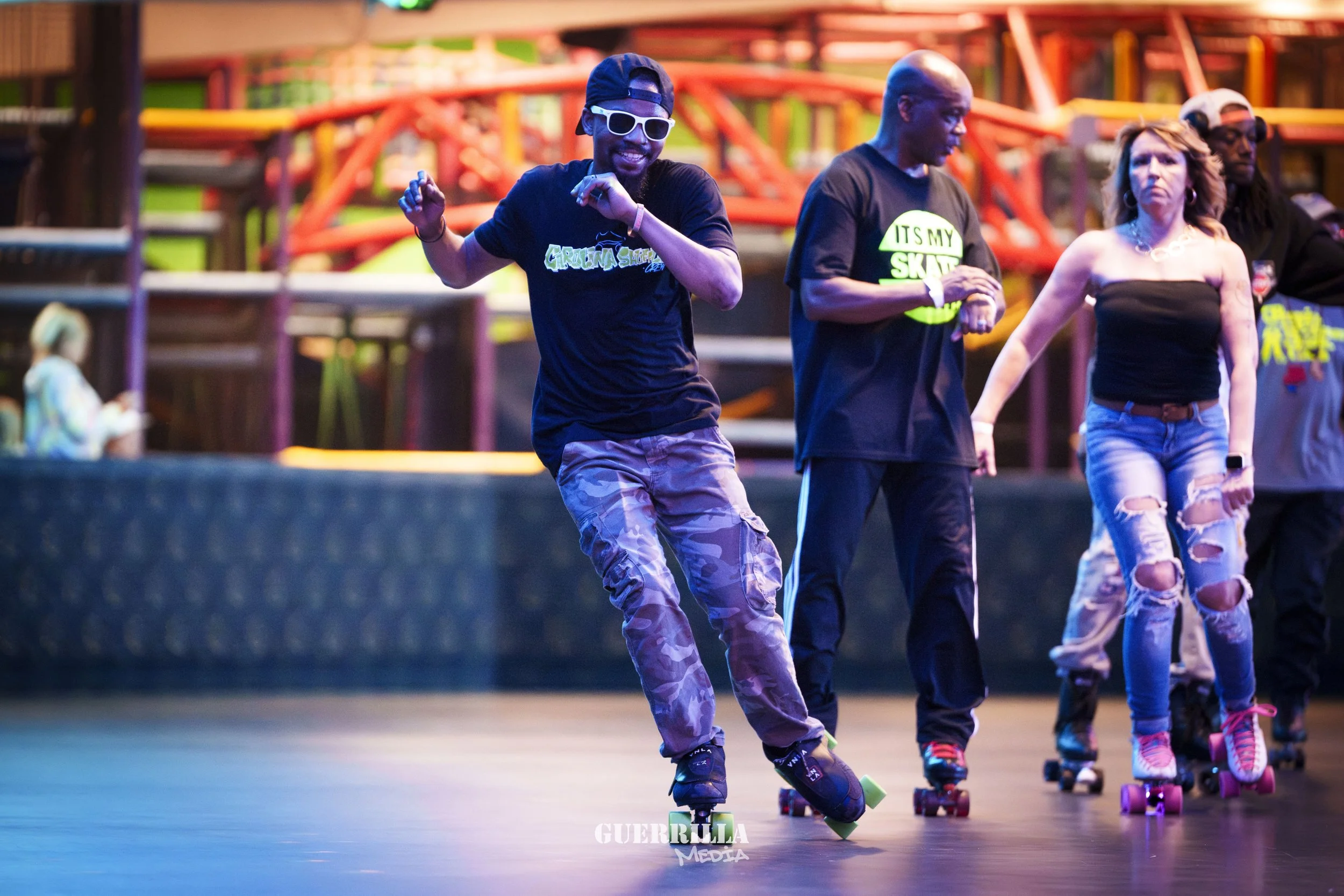 People roller skating at an indoor roller rink with colorful lights and playground equipment in the background.