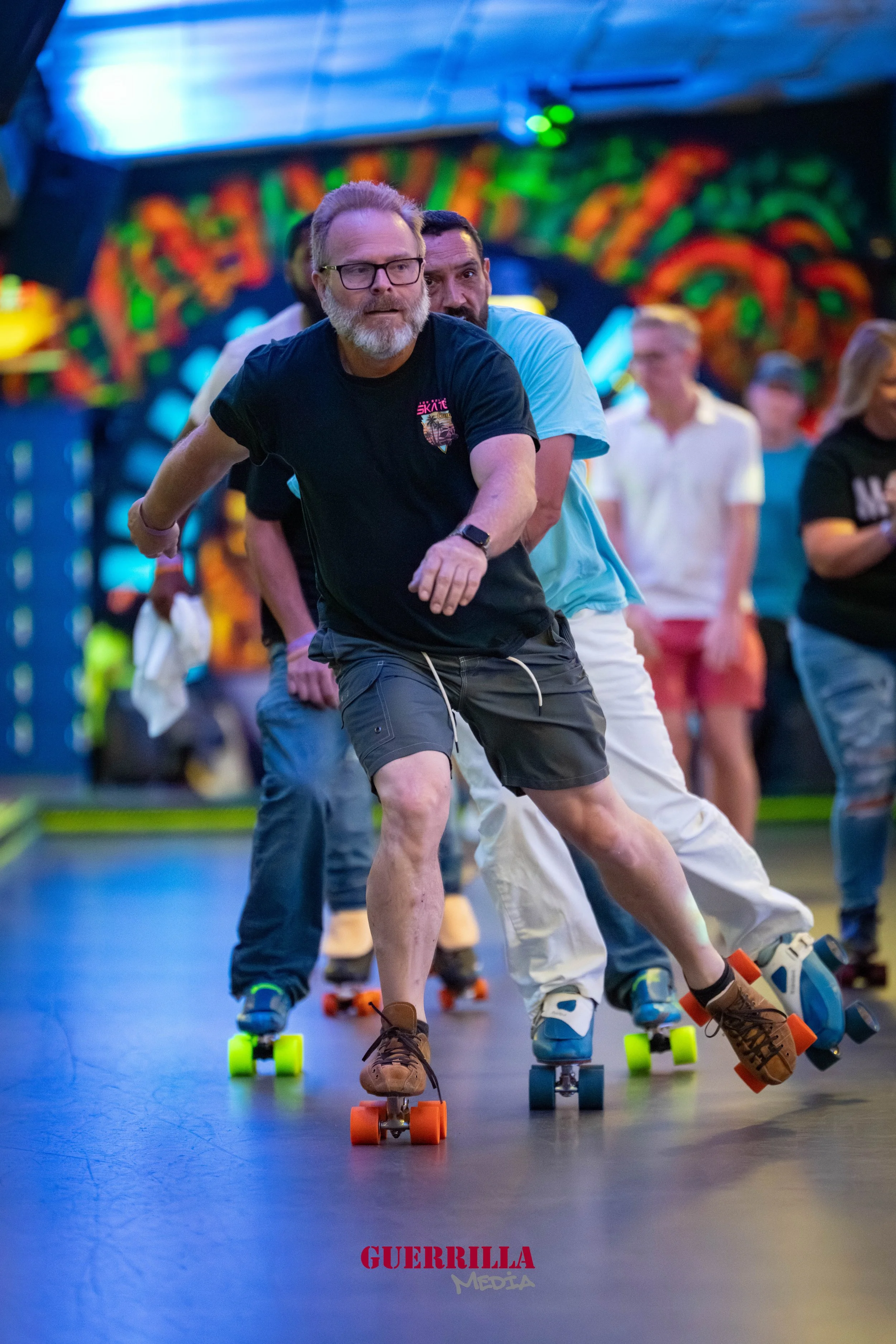 People roller skating indoors, with colorful lighting and wall art in the background.