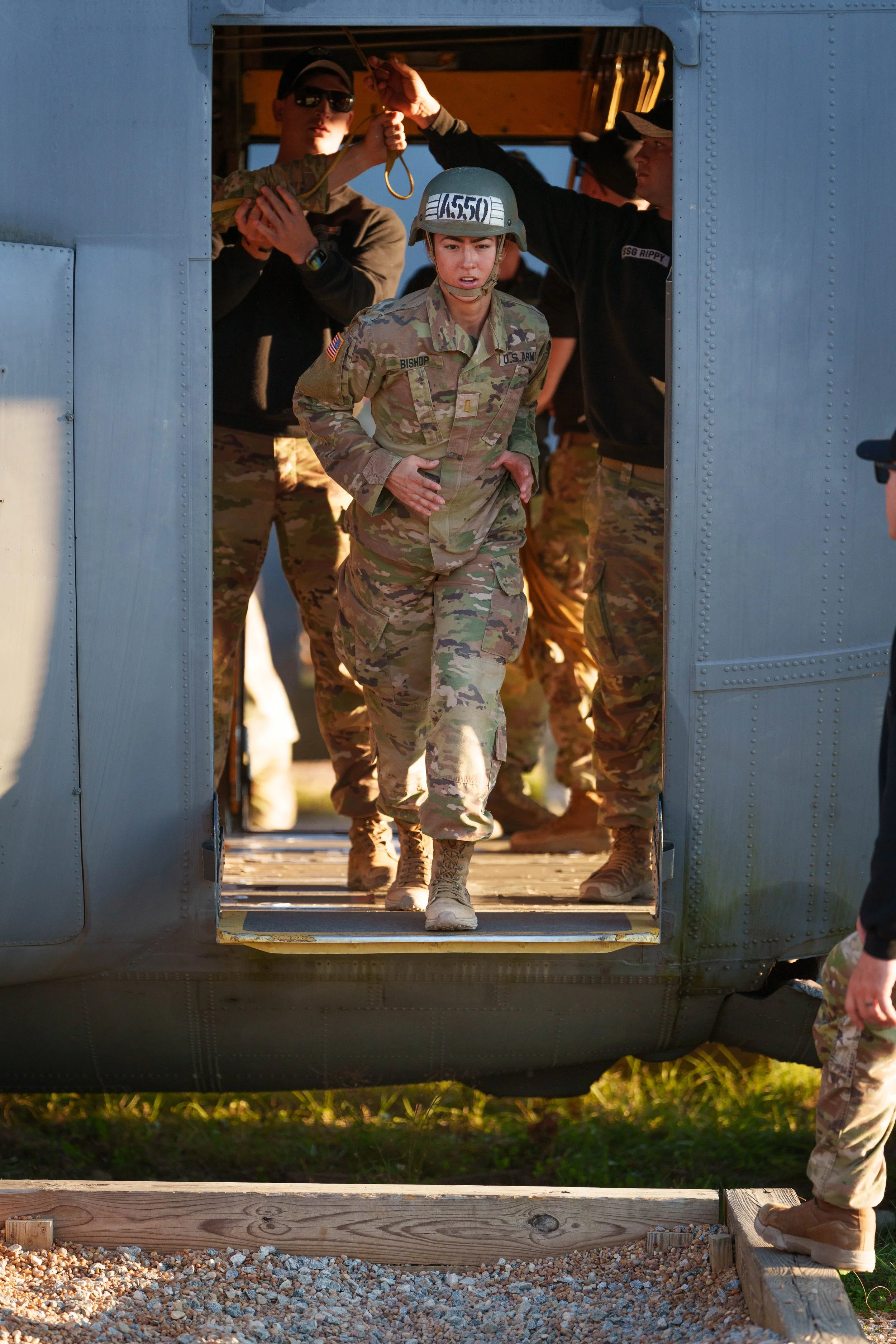 U.S. female soldier in camouflage uniform disembarking from a military helicopter during a training exercise, with other soldiers assisting.