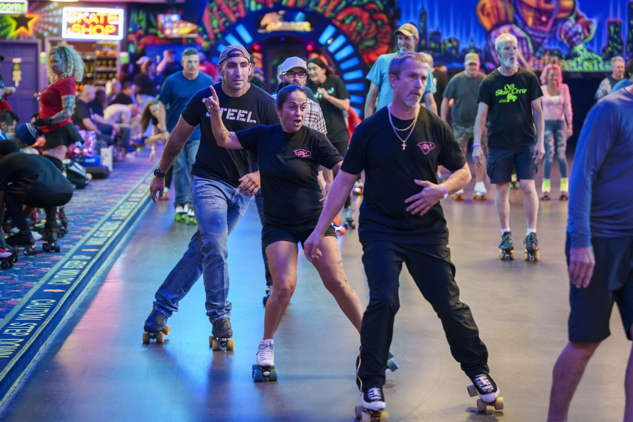People roller skating inside an arcade with colorful neon lights and a vibrant mural in the background.