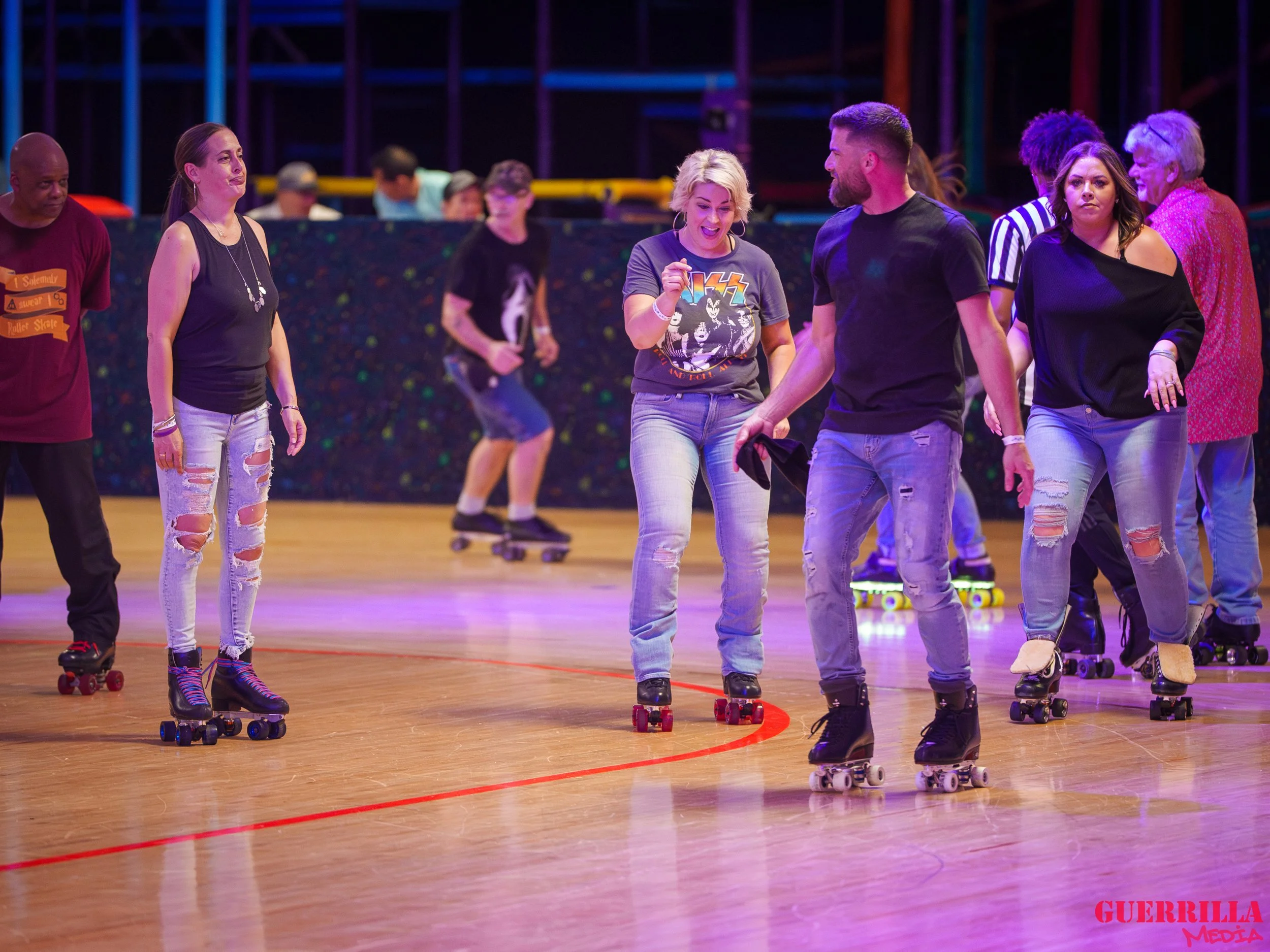 Group of people roller skating indoors, some talking, others skating, in a casual setting with colorful lighting.
