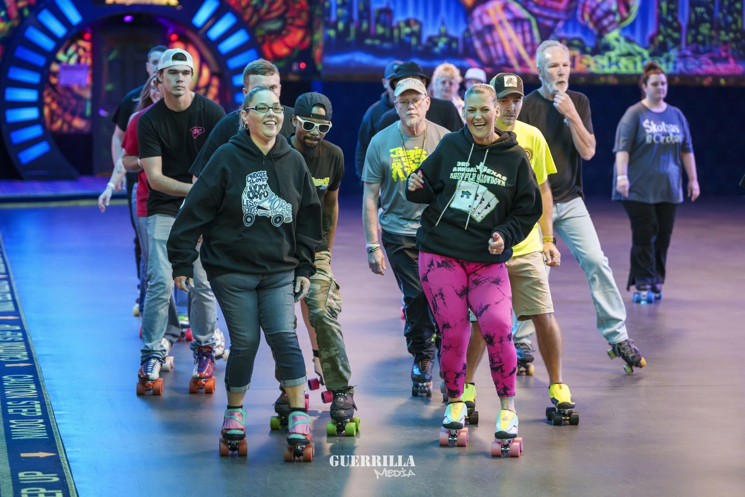 Group of people roller skating indoors, some smiling and enjoying, colorful background, advertising text on floor.