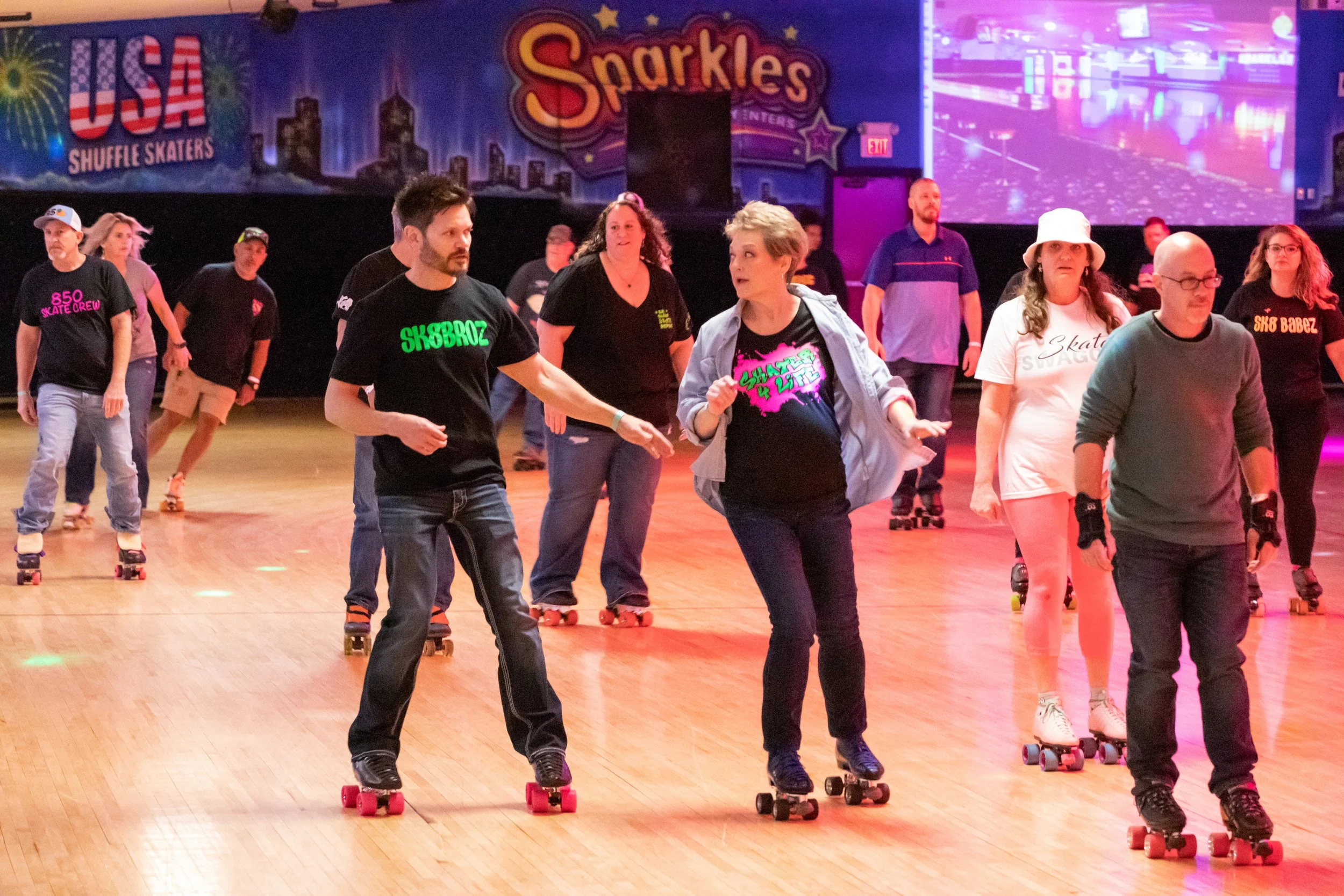 People roller skating in a rink with colorful neon lights and a backdrop featuring city skyline, 