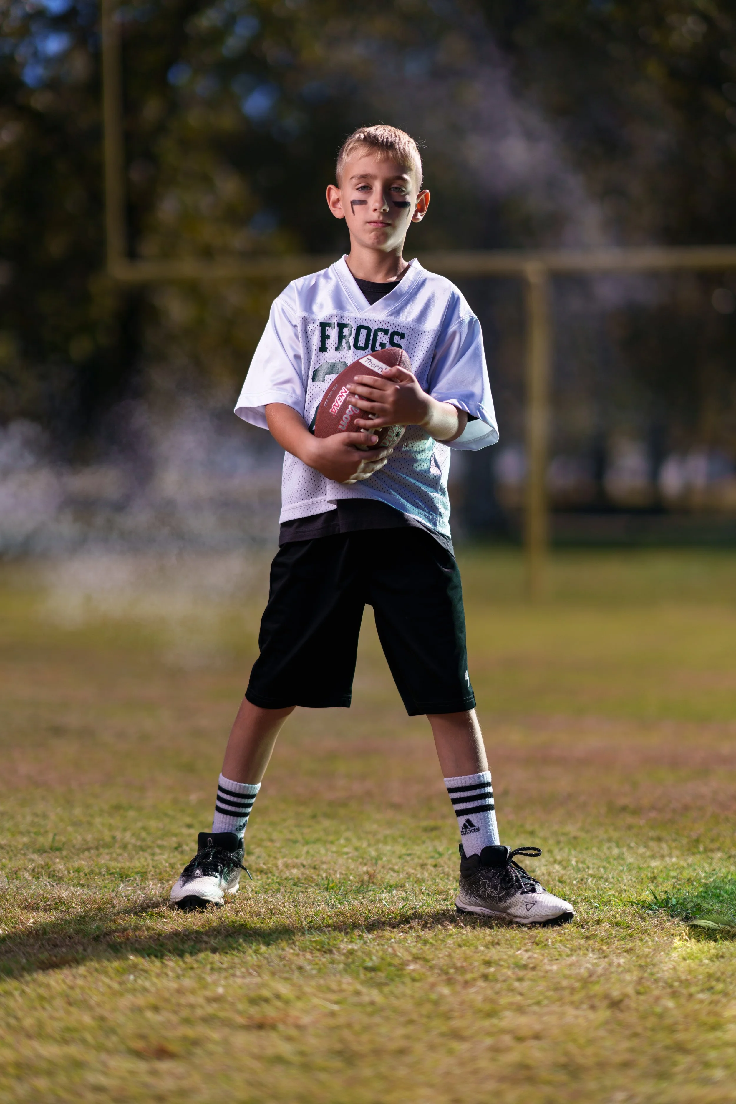 A young boy in a football uniform holding a football on a football field.