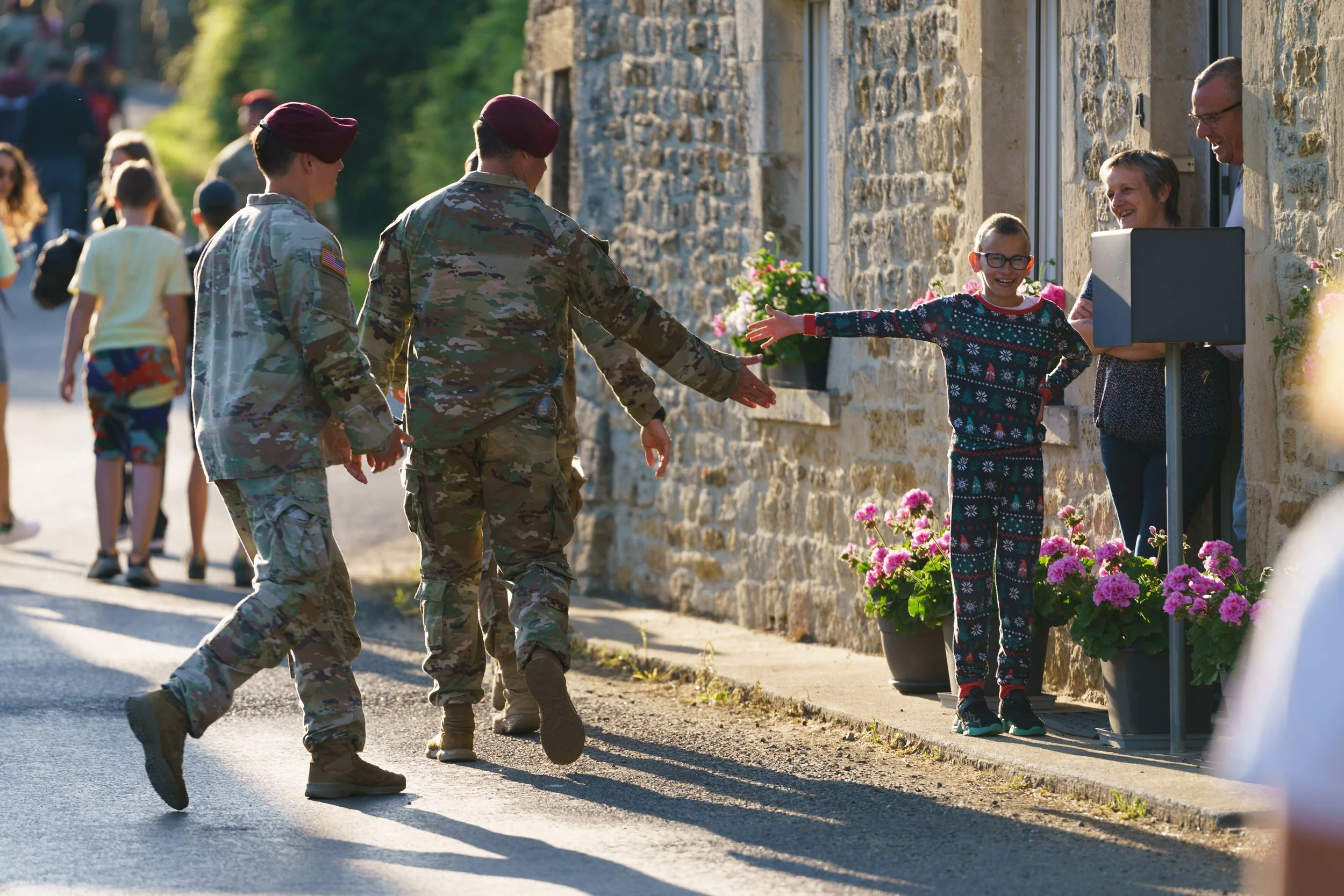 Soldiers in uniform greeting civilians outside a stone building with pink flowers.