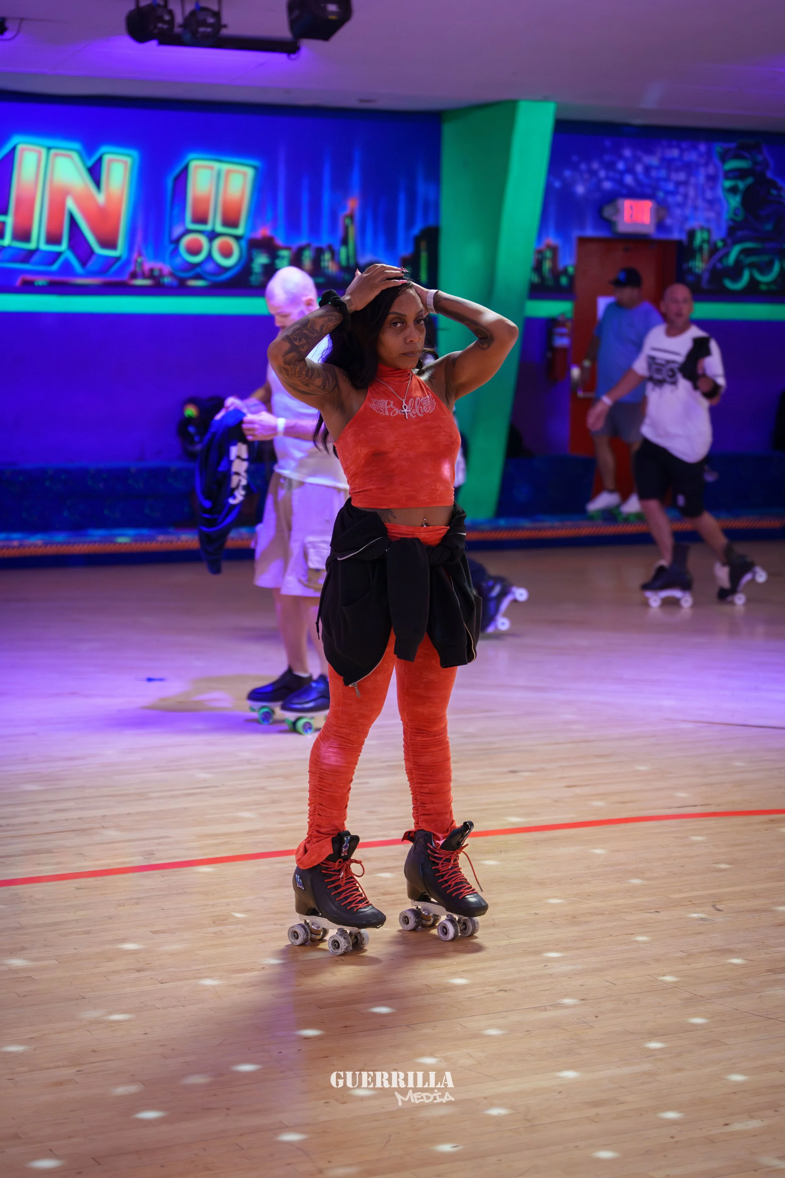 A woman wearing red rollerblades and matching red clothing on a roller-skating rink, with her hands on her head.