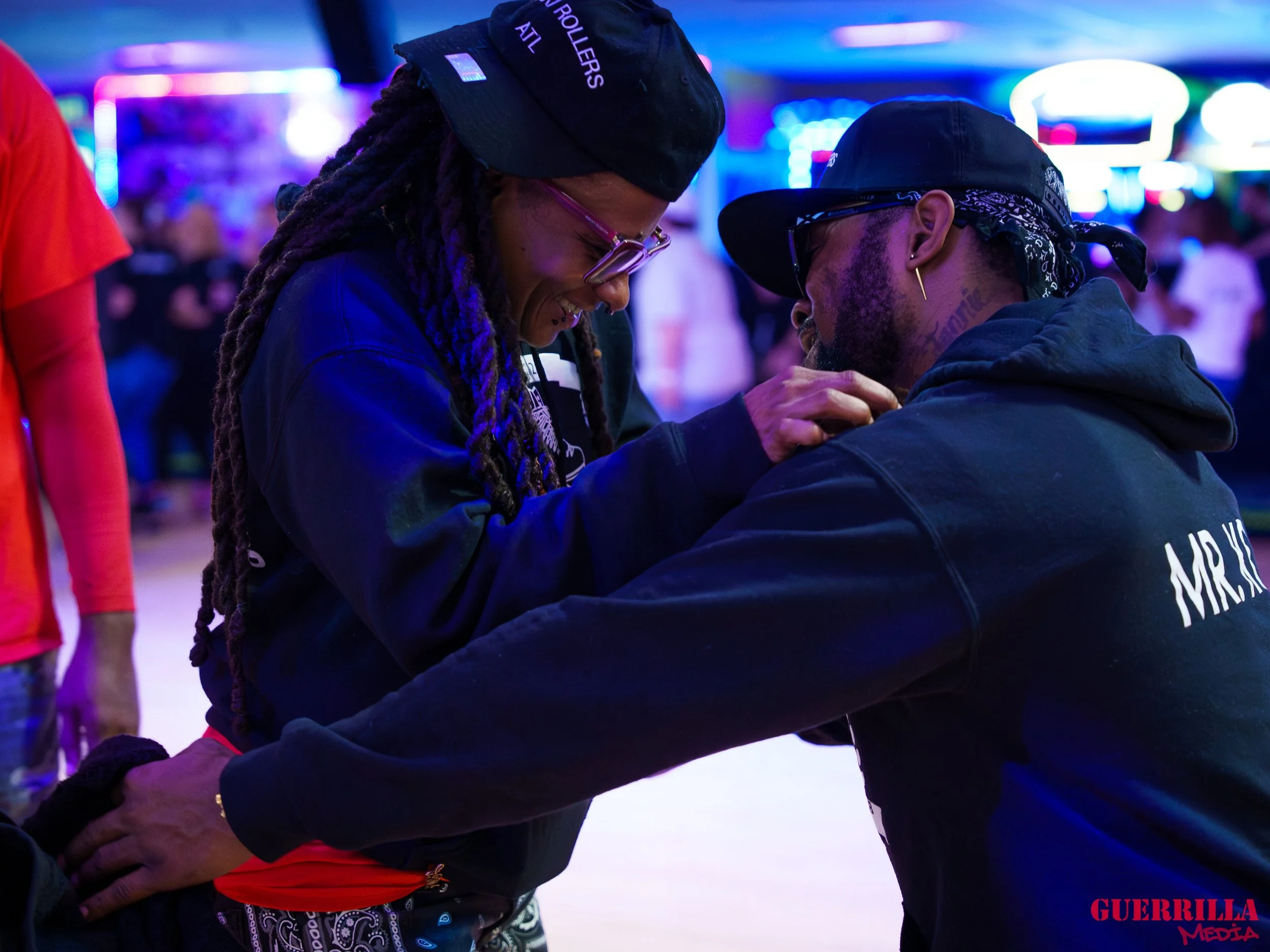 A woman and a man are roller skating together in a rink decorated with neon lights. They are smiling and laughing, holding hands, and appear to be having fun.