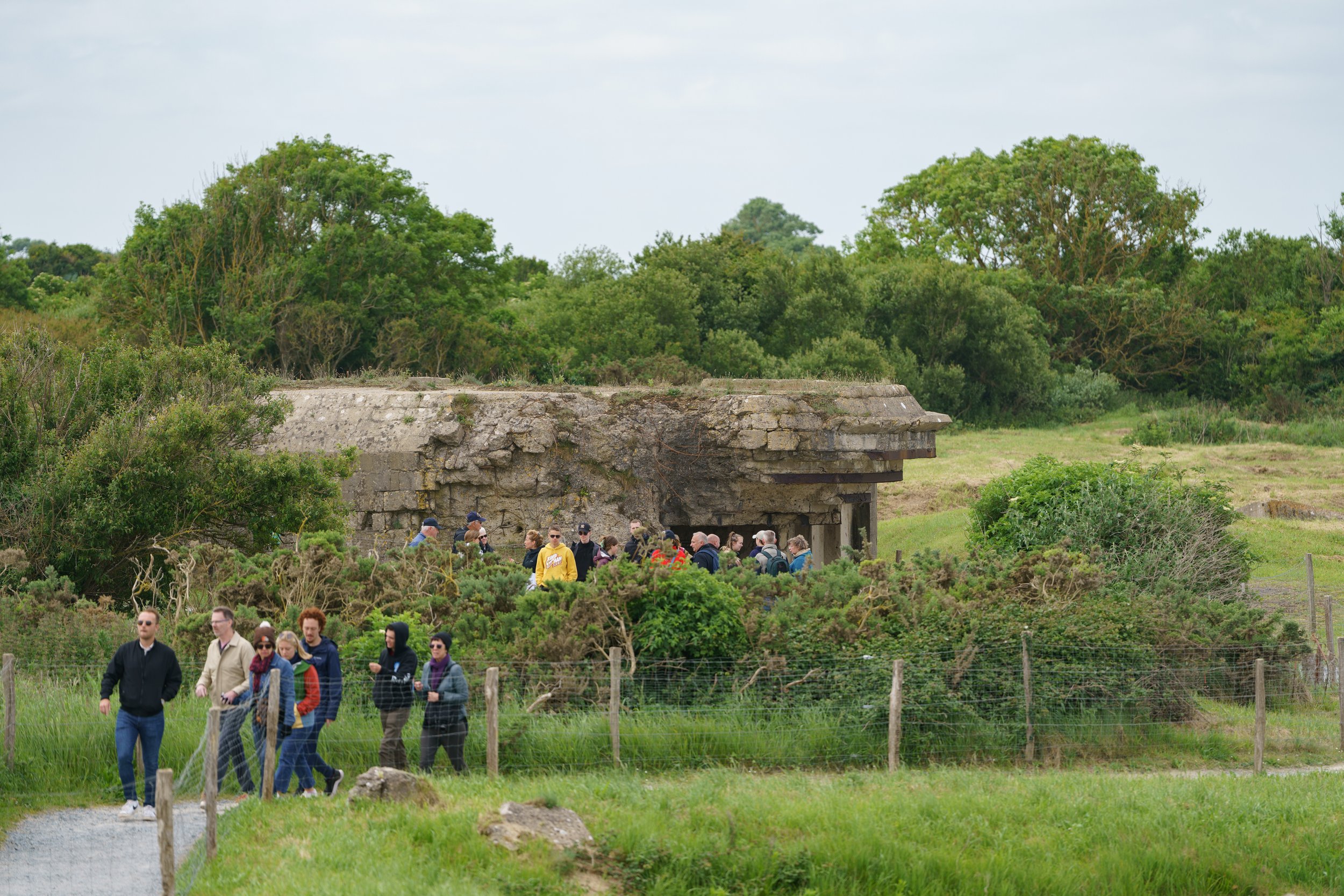 Group of tourists walking and gathering near a historic stone structure surrounded by greenery.
