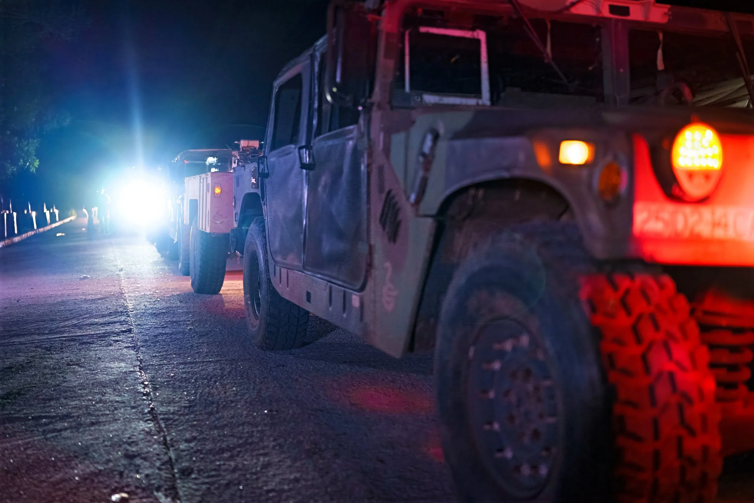 Line of military vehicles at night with flashing lights.