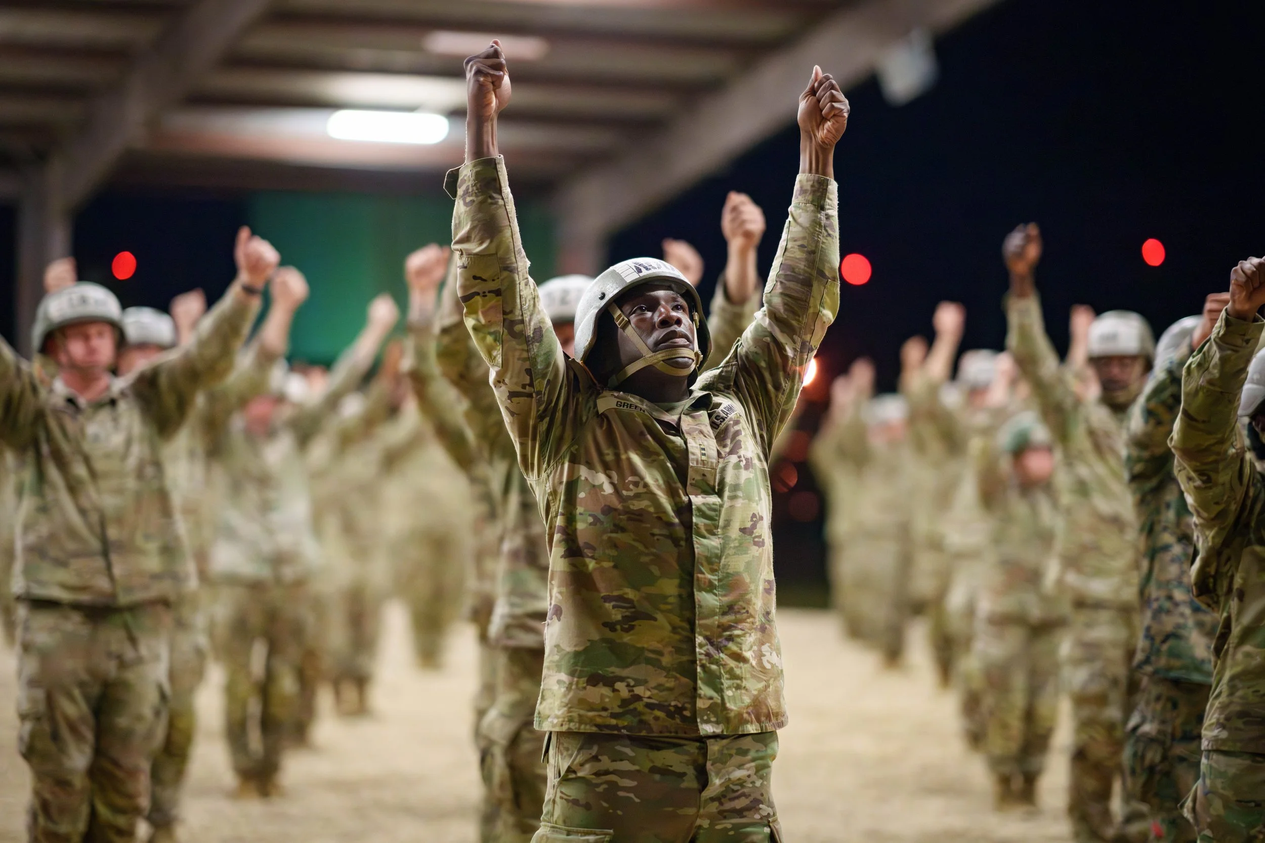 Group of soldiers in camouflage uniforms standing in formation with hands raised.