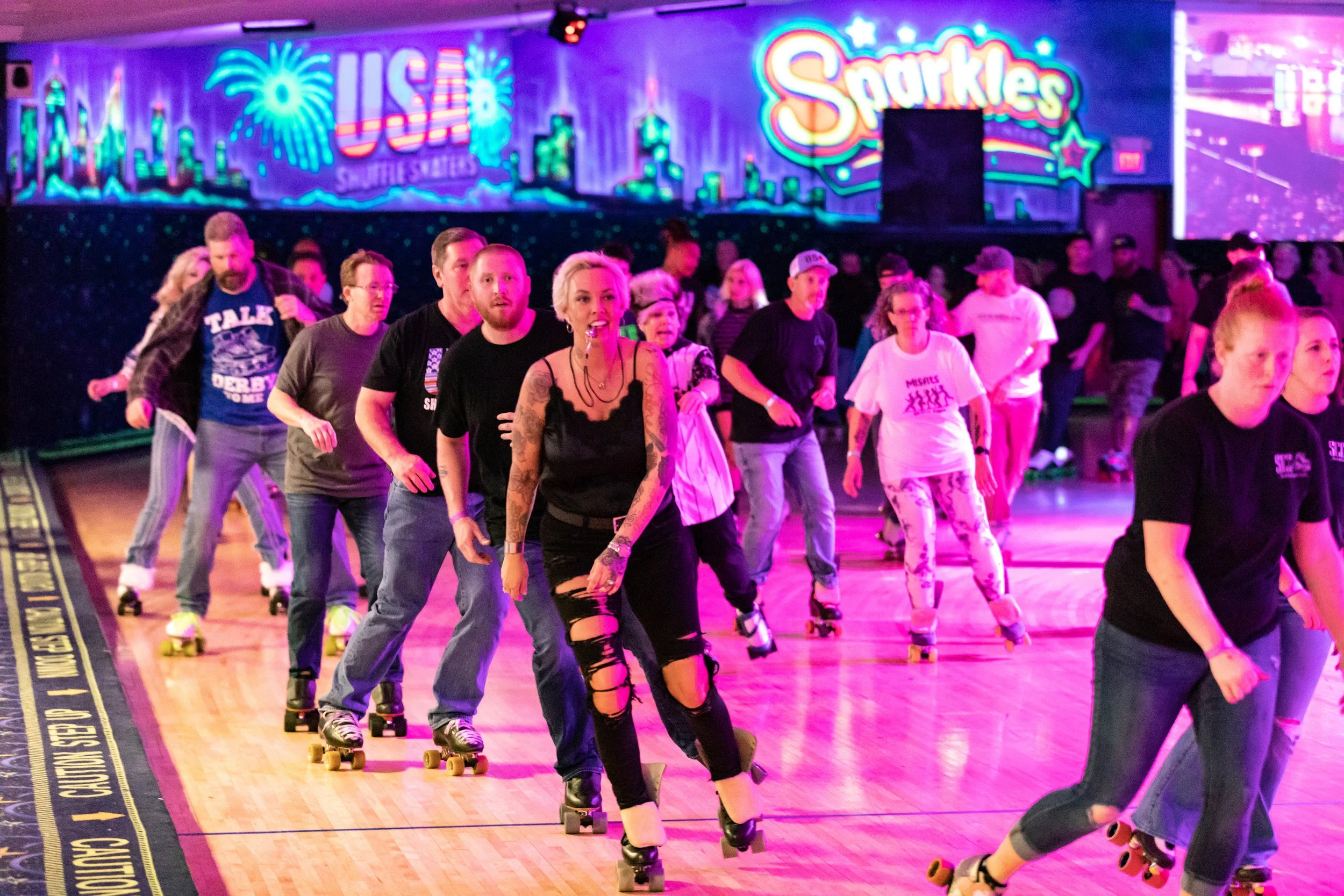 Group of people roller skating indoors under neon lights with colorful signs that say "USAF" and "Sparkles."