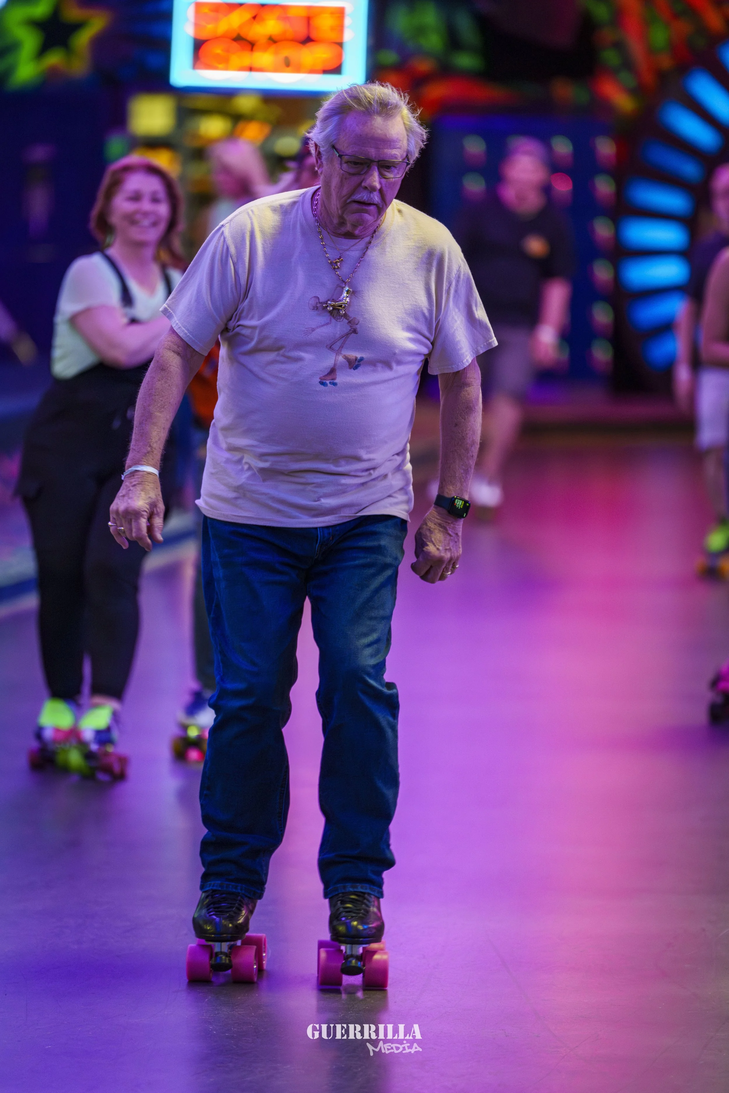 Older man roller skating indoors at an arcade or roller rink, with colorful neon lights and other skaters in the background.