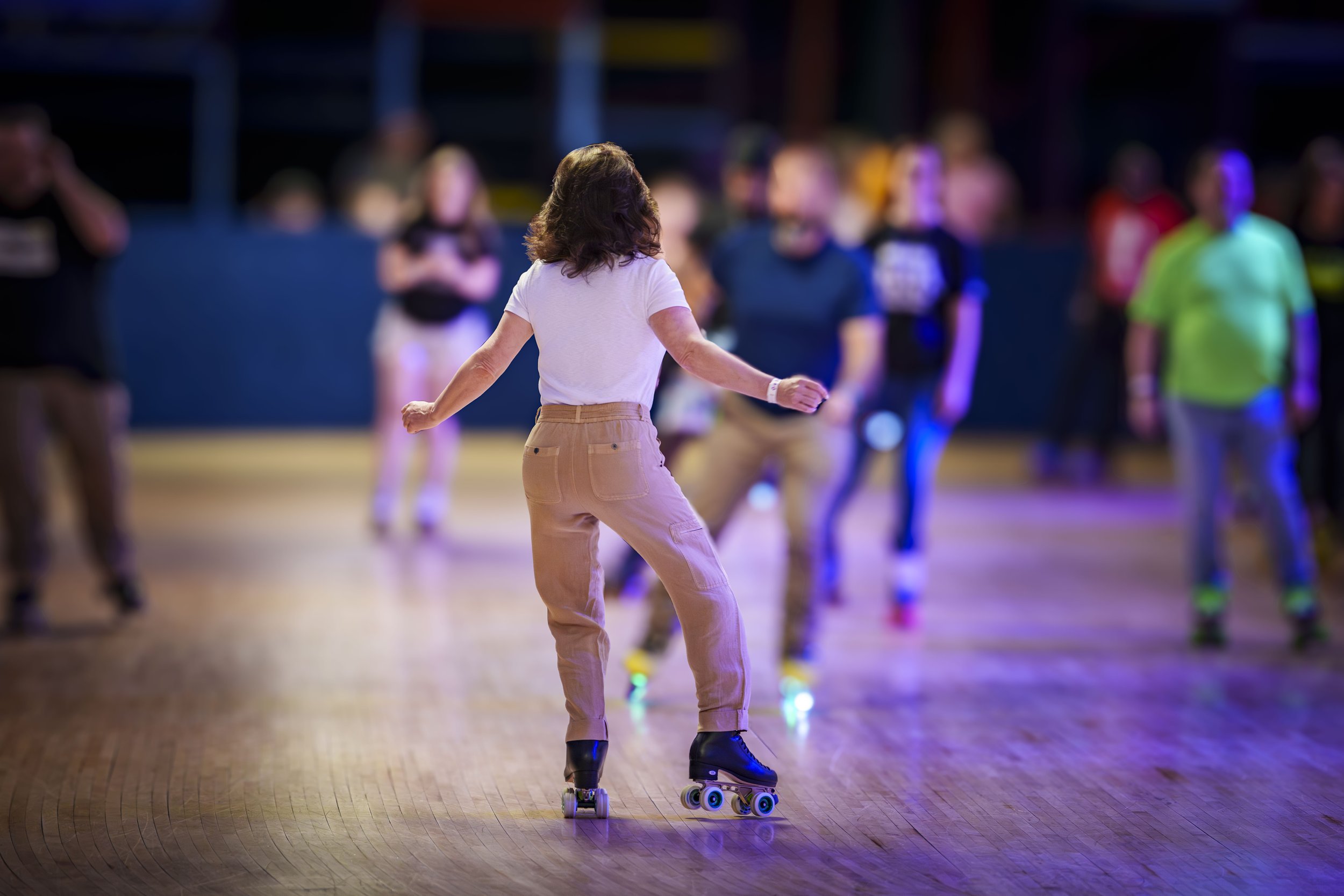 A woman roller skating in a rink with a group of people in the background.