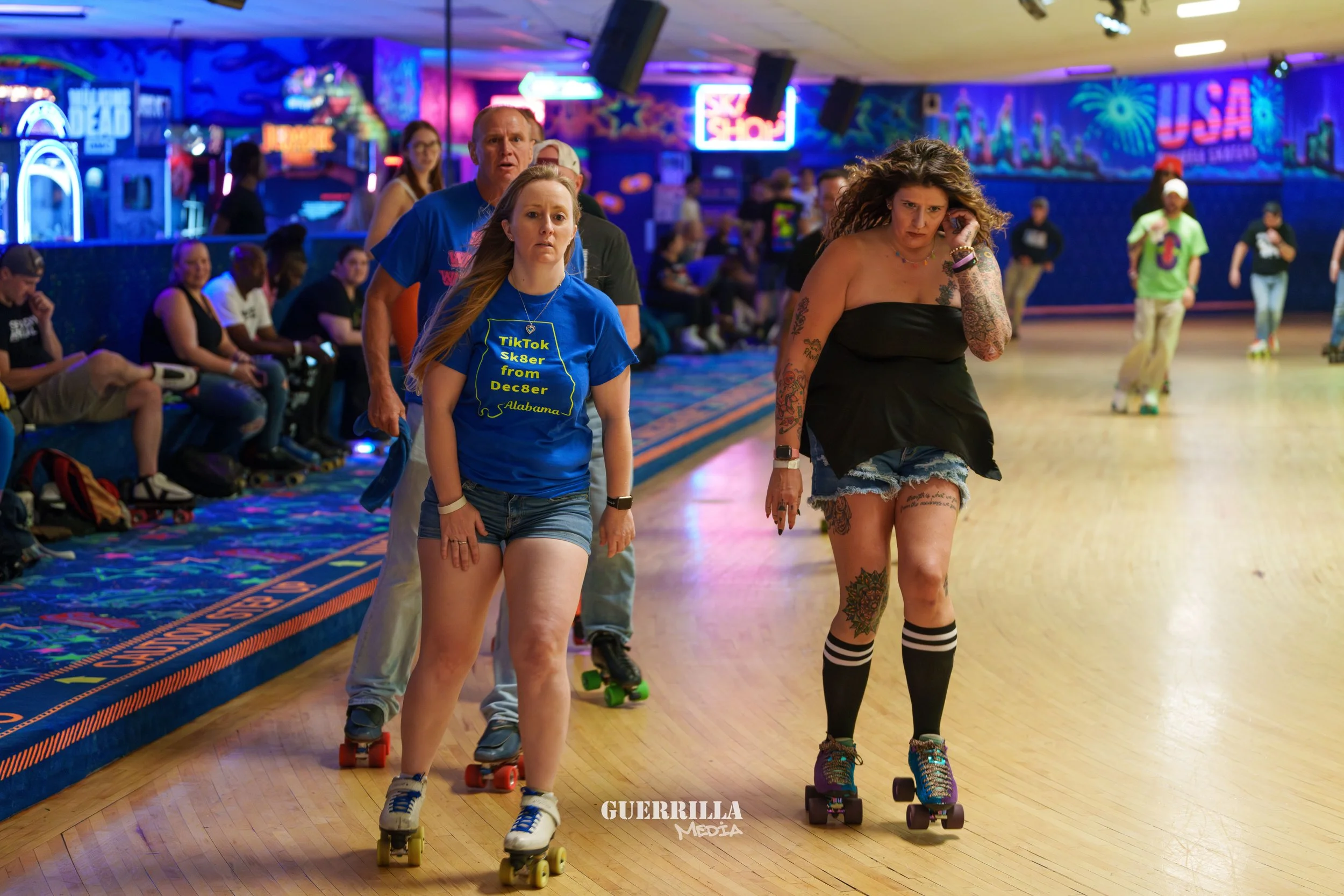 People roller skating at an indoor rink with neon lights and colorful mural artwork in the background.