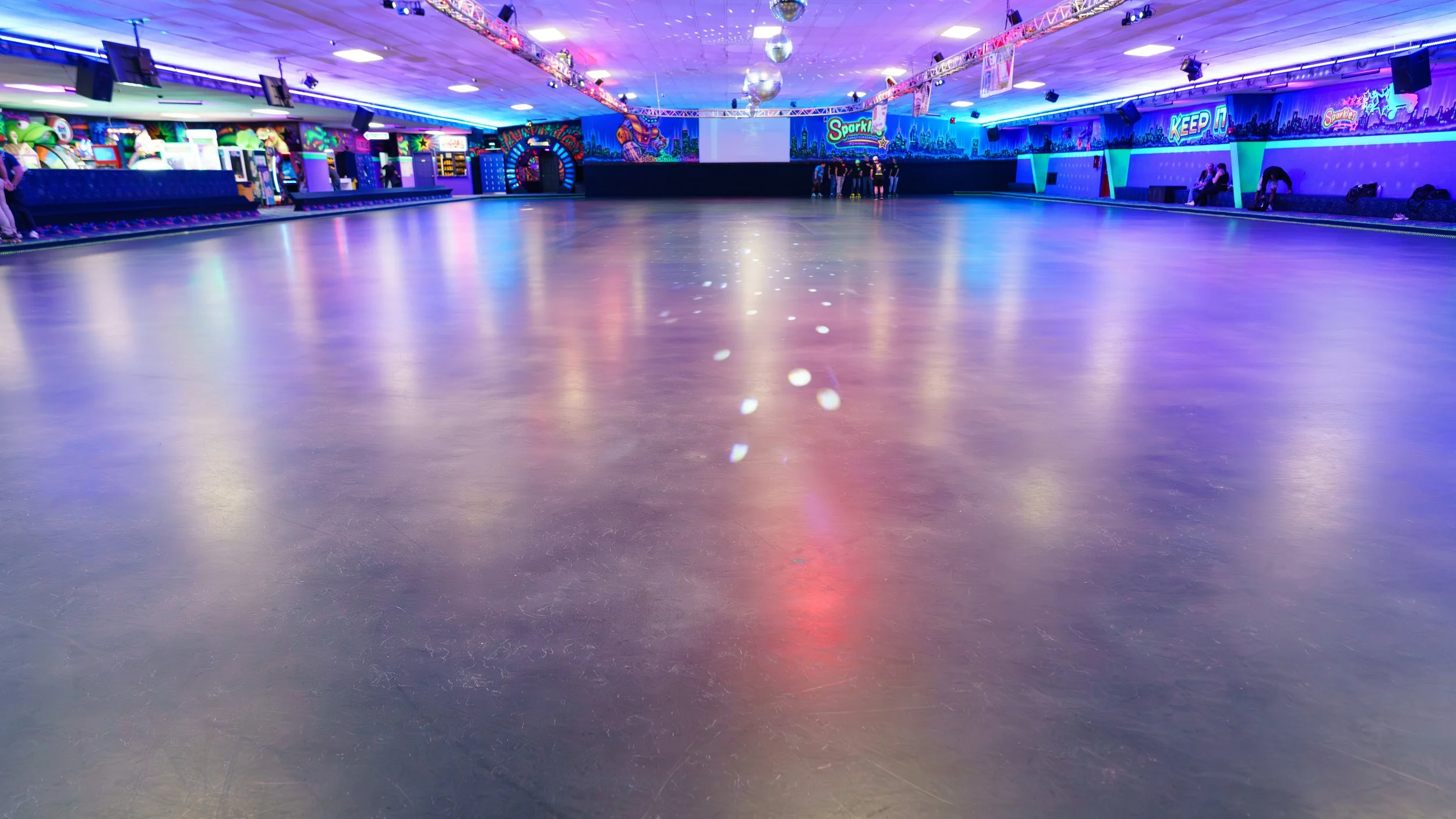 Empty indoor roller skating rink with colorful neon lights and arcade games along the walls.