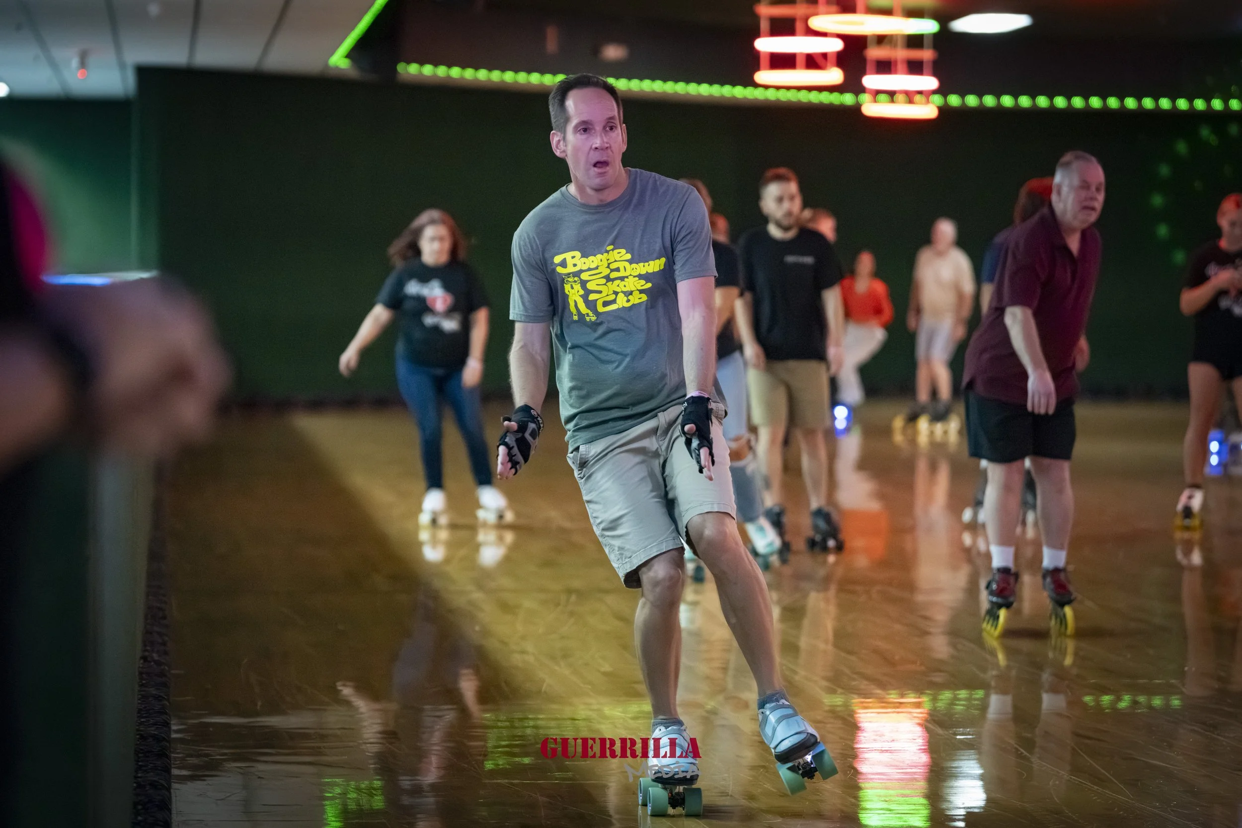 People roller skating indoors on a polished wooden floor under neon lighting.