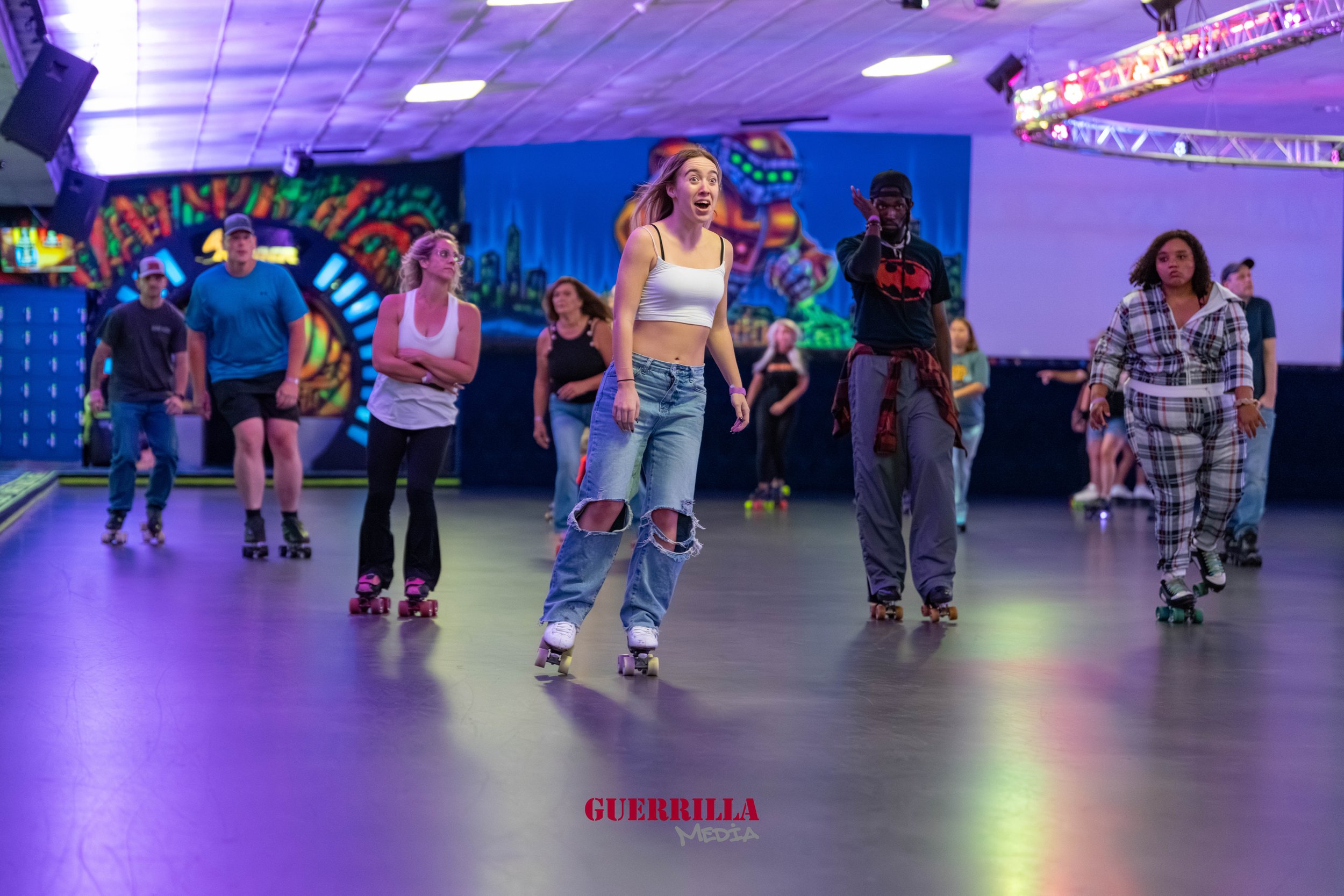 People roller skating inside a colorful, neon-lit roller rink.