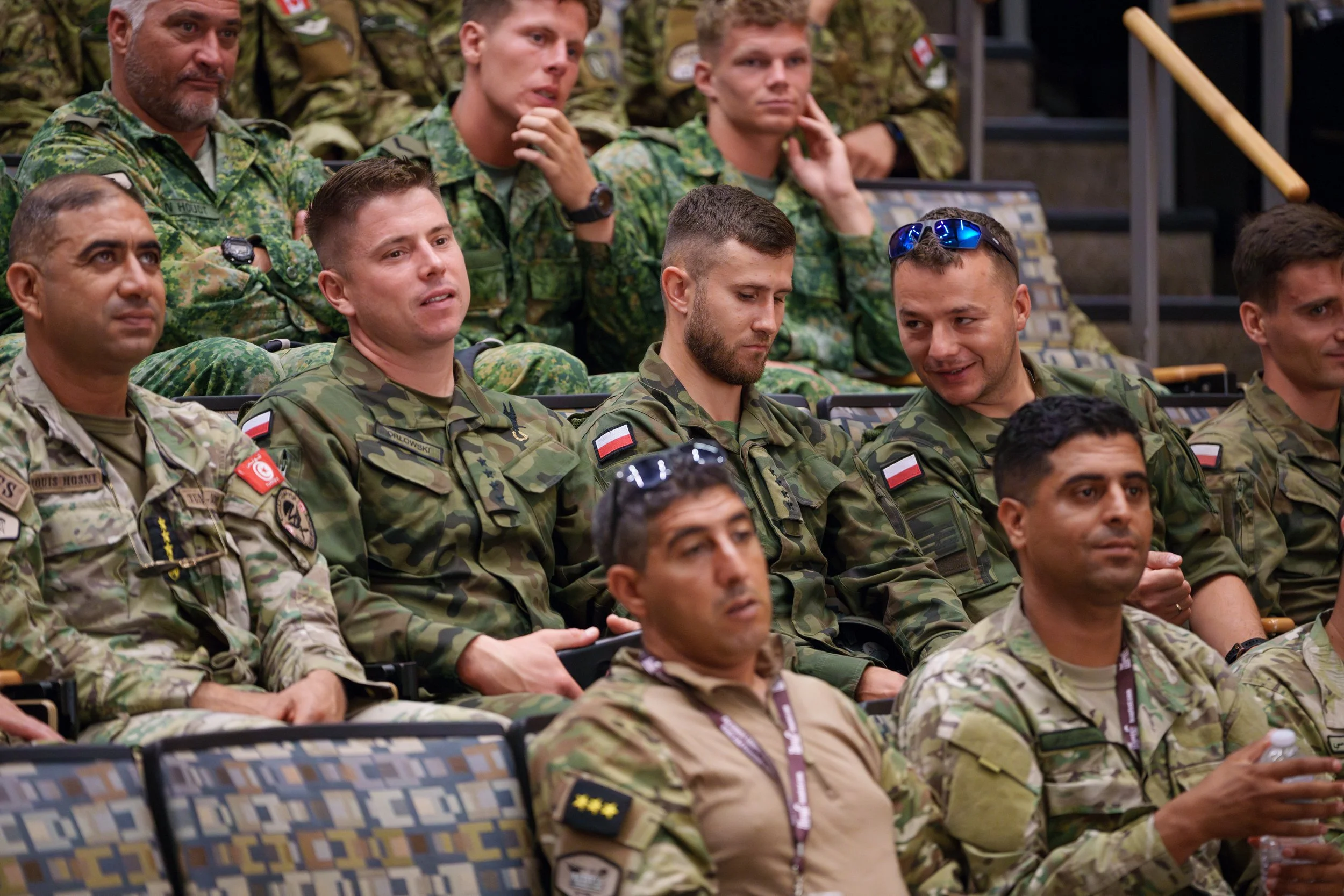 Group of soldiers in camouflage uniforms attending a presentation or briefing in an auditorium.