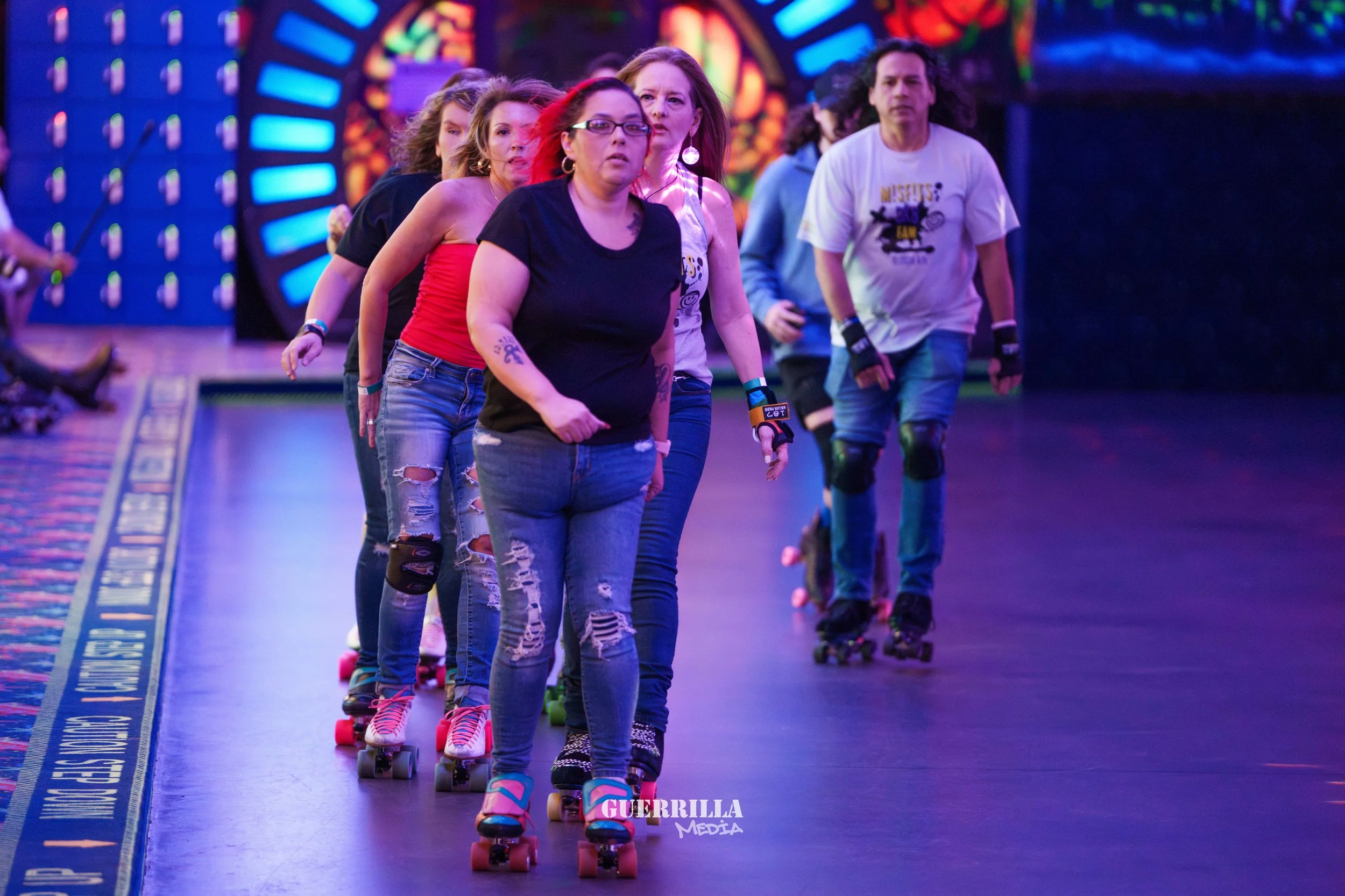 People roller skating indoors with colorful, stained glass window decorations in the background.